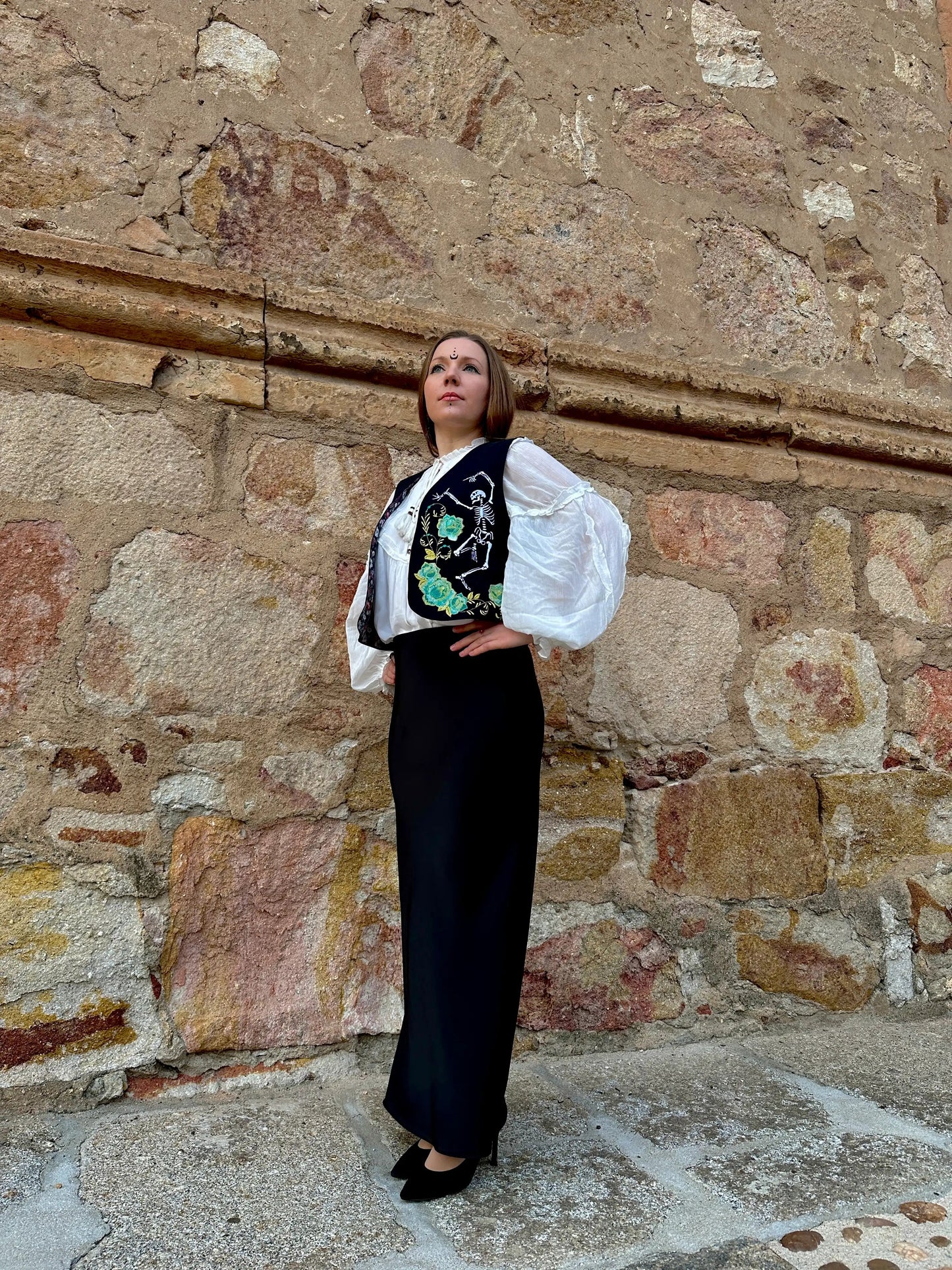 Woman in a stylish outfit standing against a stone wall.