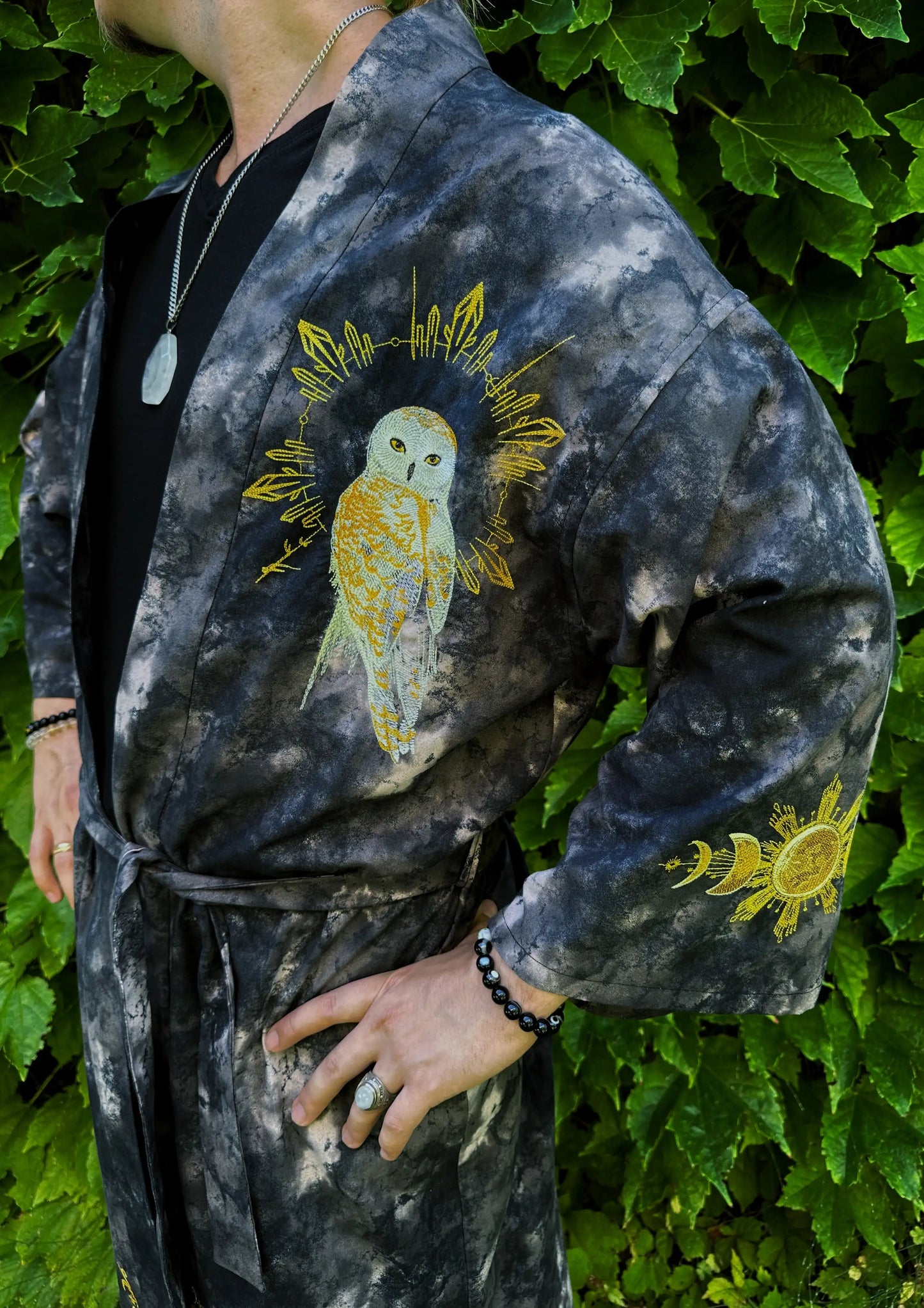 Person wearing a dark robe with gold owl designs against a green leafy background