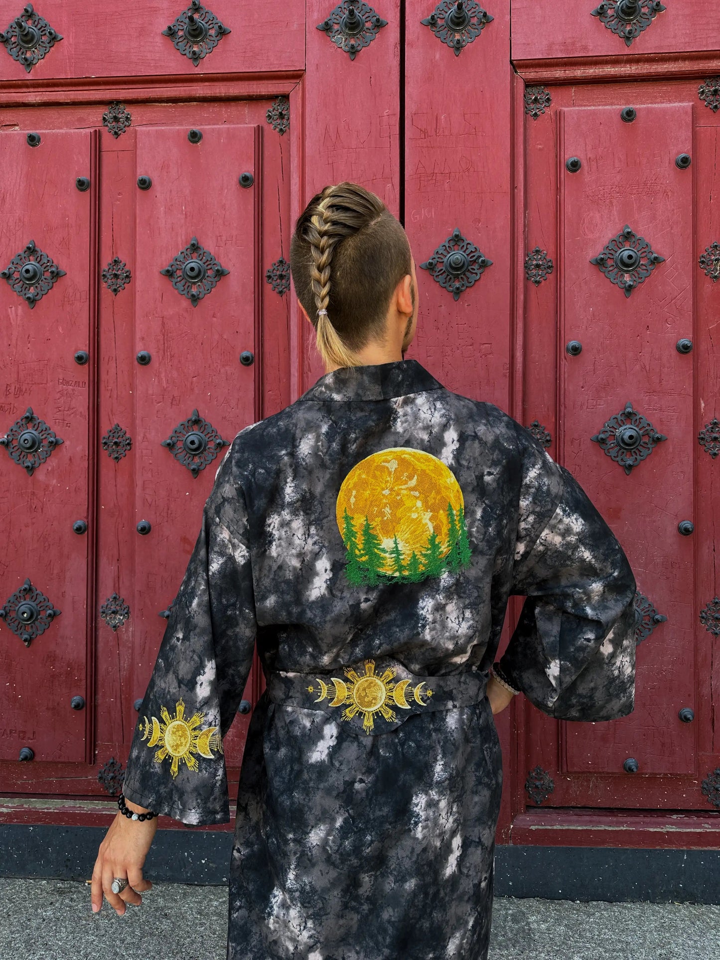 Person wearing a black tie-dye kimono with a sun design in front of a red door.