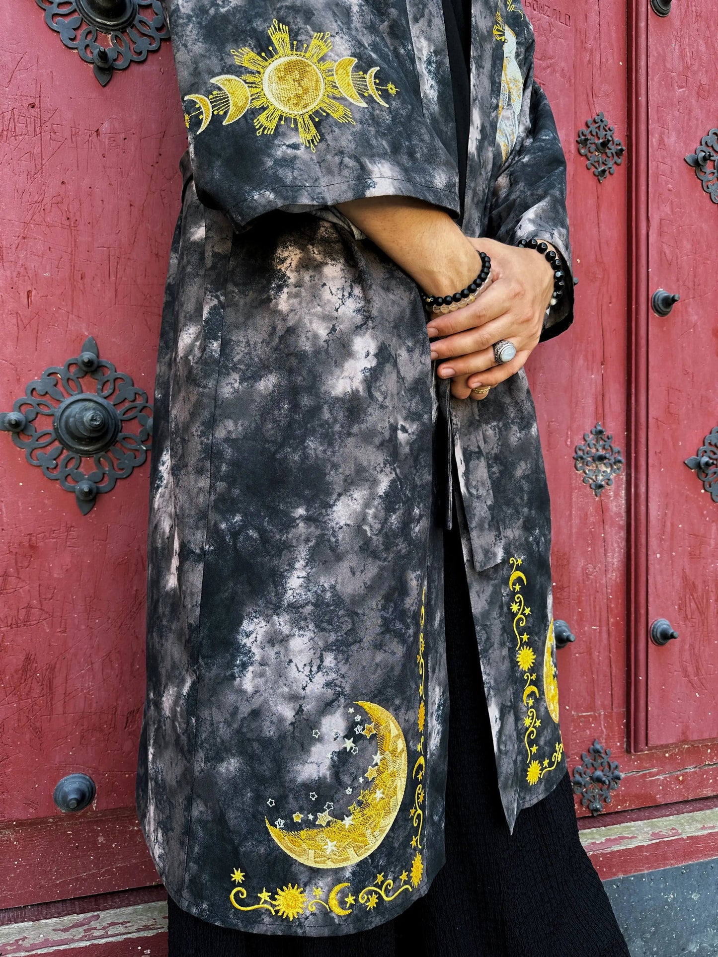 Person wearing a dark gray coat with yellow celestial designs in front of a red door.