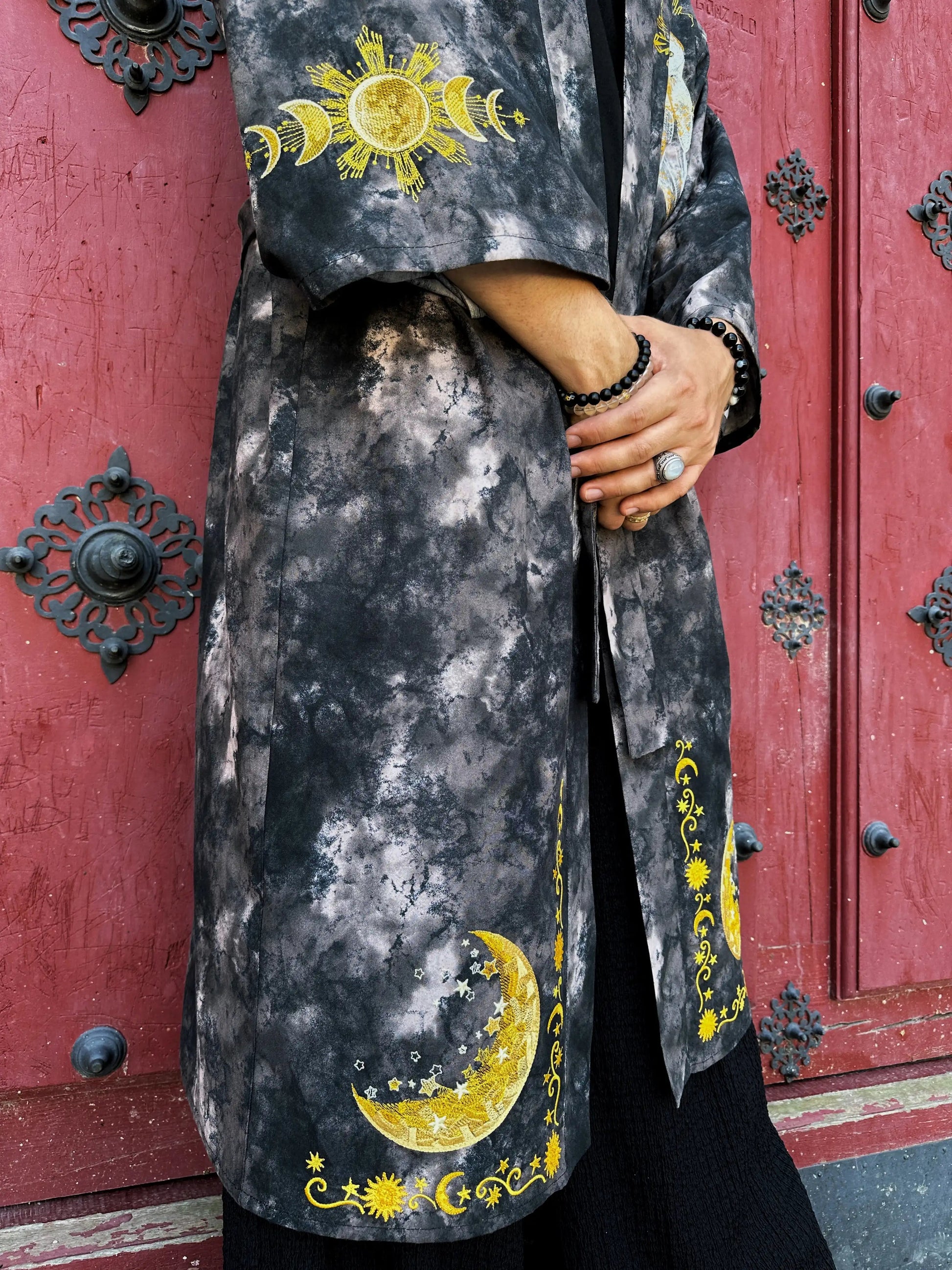 Person wearing a dark gray coat with yellow celestial designs in front of a red door.