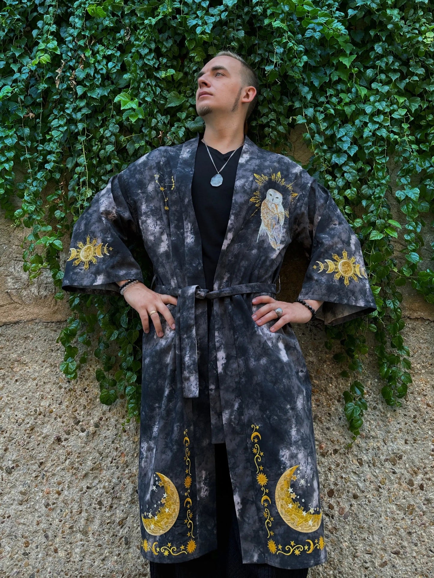 Person wearing a dark robe with yellow patterns against a green ivy-covered wall.