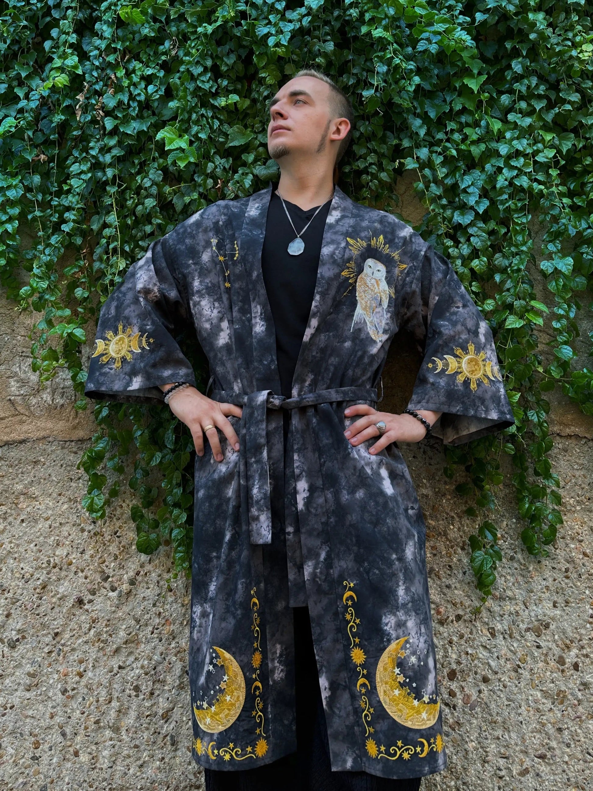 Person wearing a dark robe with yellow patterns against a green ivy-covered wall.