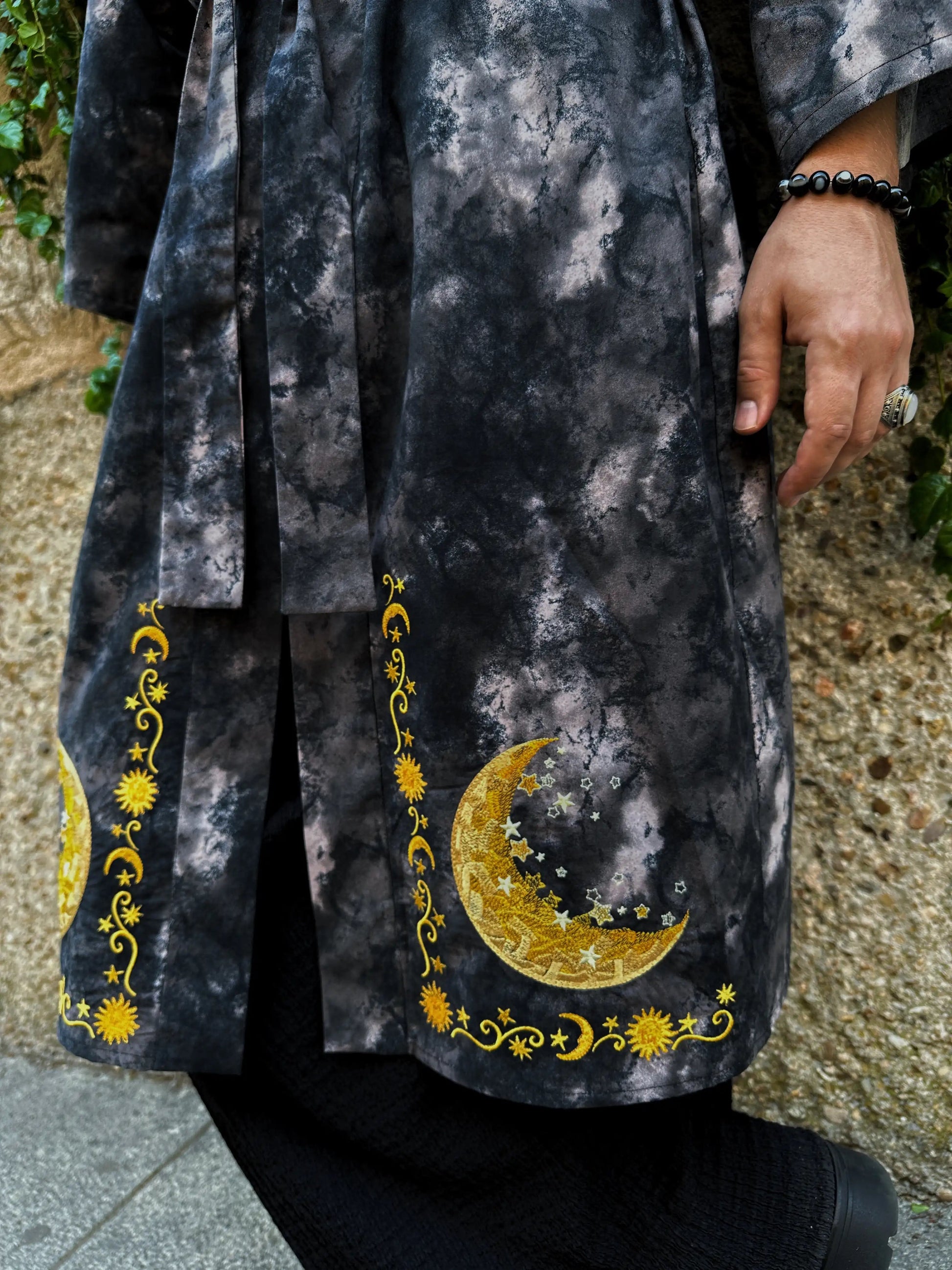 Black and gray tie-dye garment with gold moon and star designs on a textured surface.