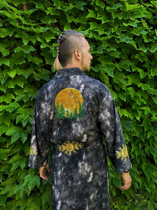 Person wearing a dark jacket with sun and tree design against a green leafy background