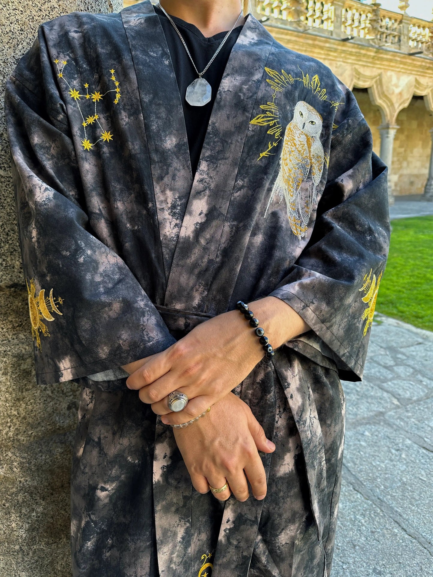 Person wearing a dark robe with owl designs outdoors.