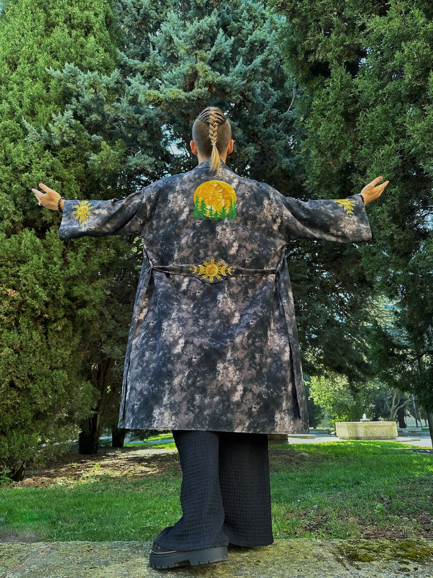 Person wearing a long coat with a floral design on the back, standing in a park.