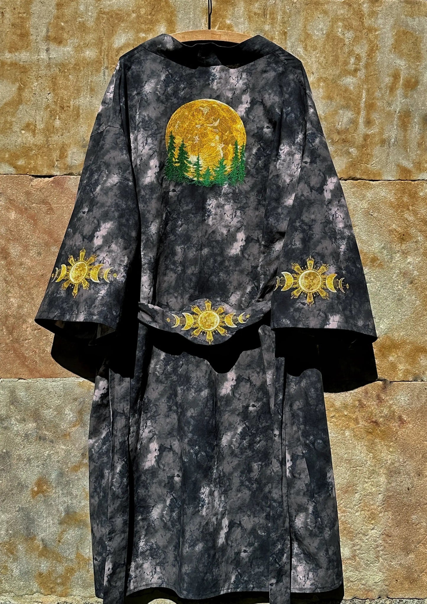 Dark robe with embroidered yellow and green designs on a textured stone wall background