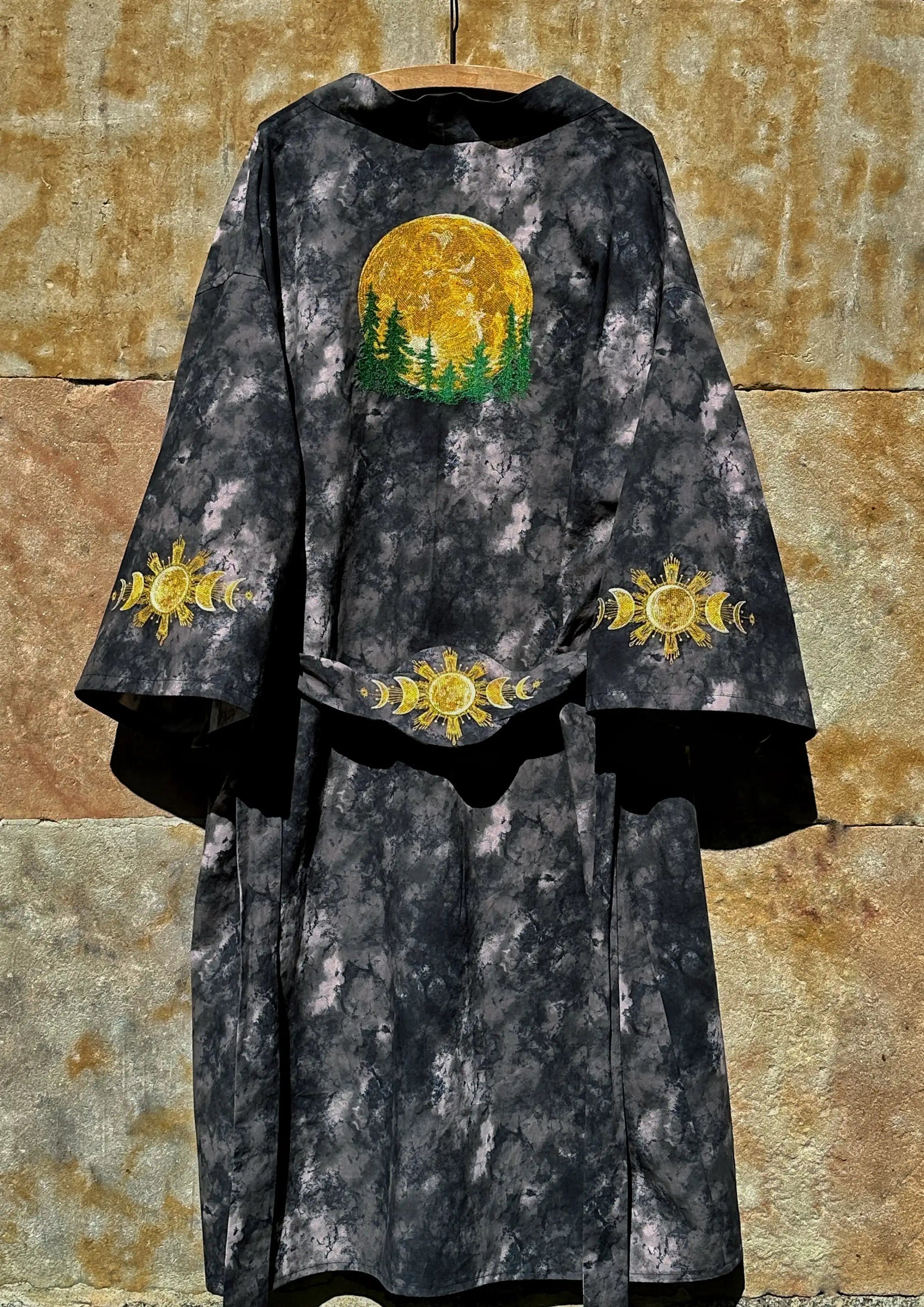 Dark robe with embroidered yellow and green designs on a textured stone wall background