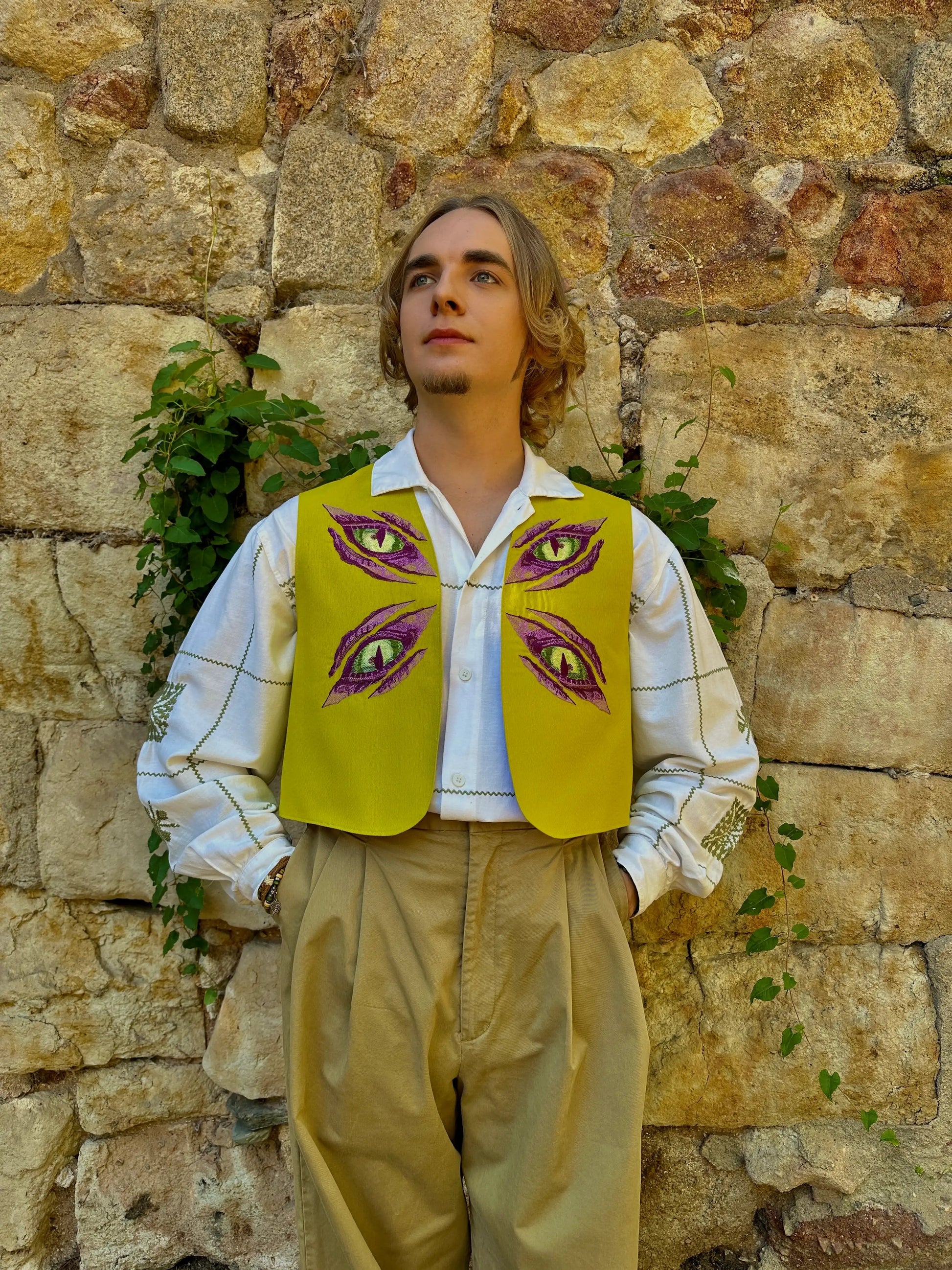 Person wearing a yellow vest with eye designs against a stone wall.