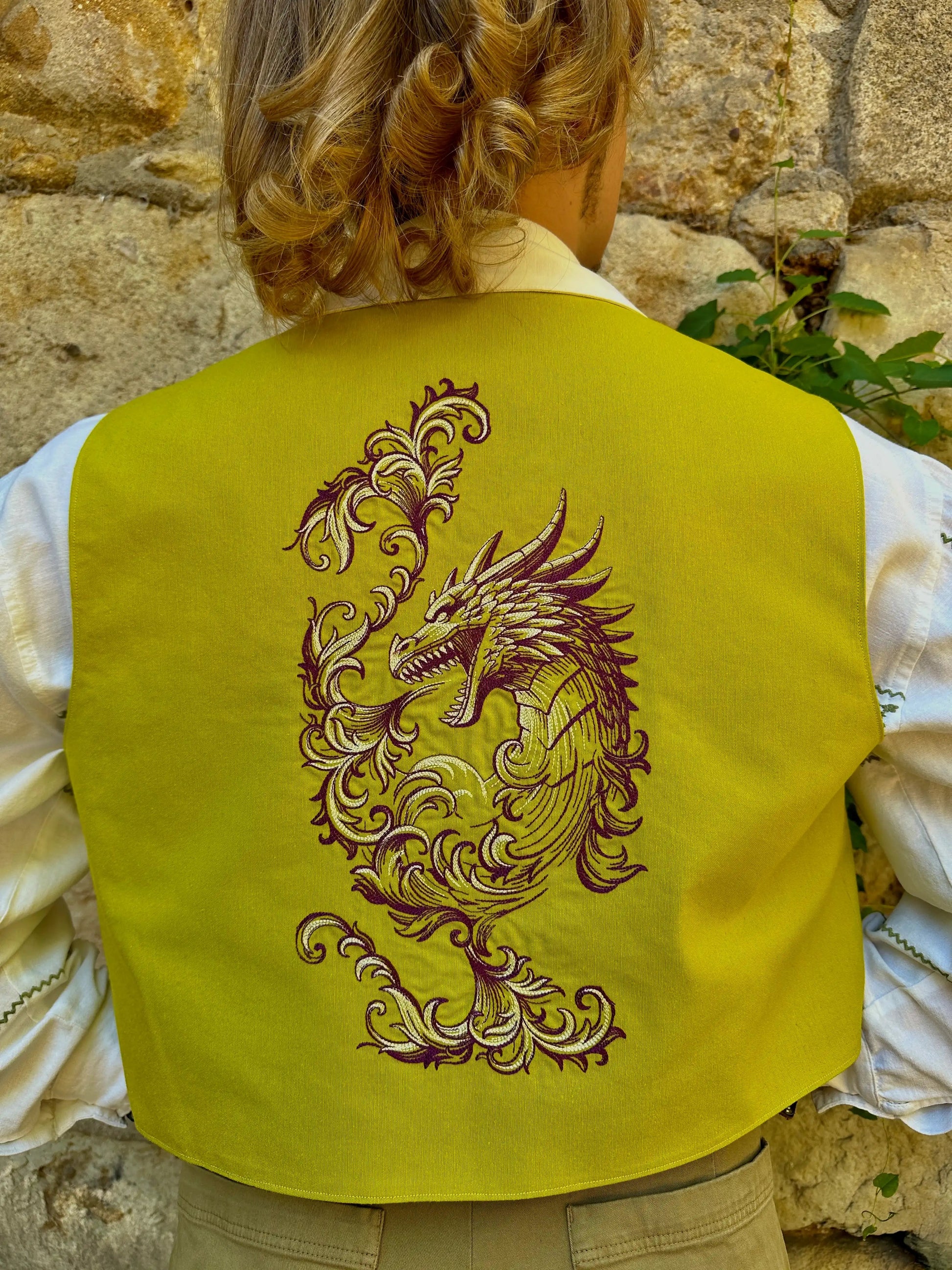 Person wearing a yellow vest with a dragon design against a stone wall background