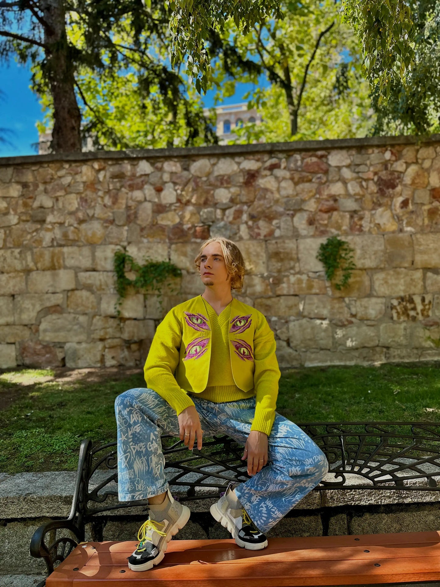 Person sitting on a bench in a park with a stone wall and greenery in the background