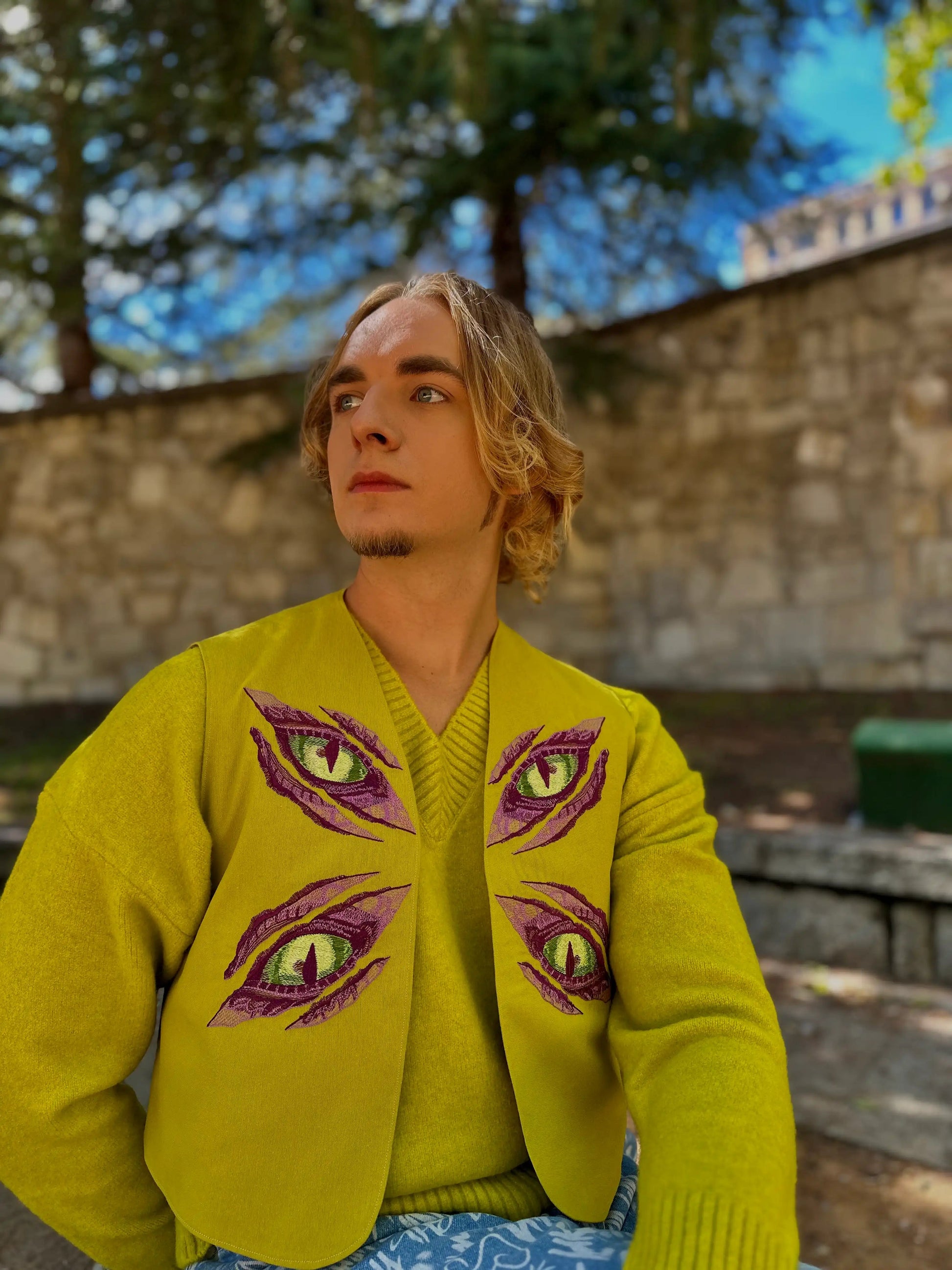 Person wearing a bright green sweater with eye designs outdoors.