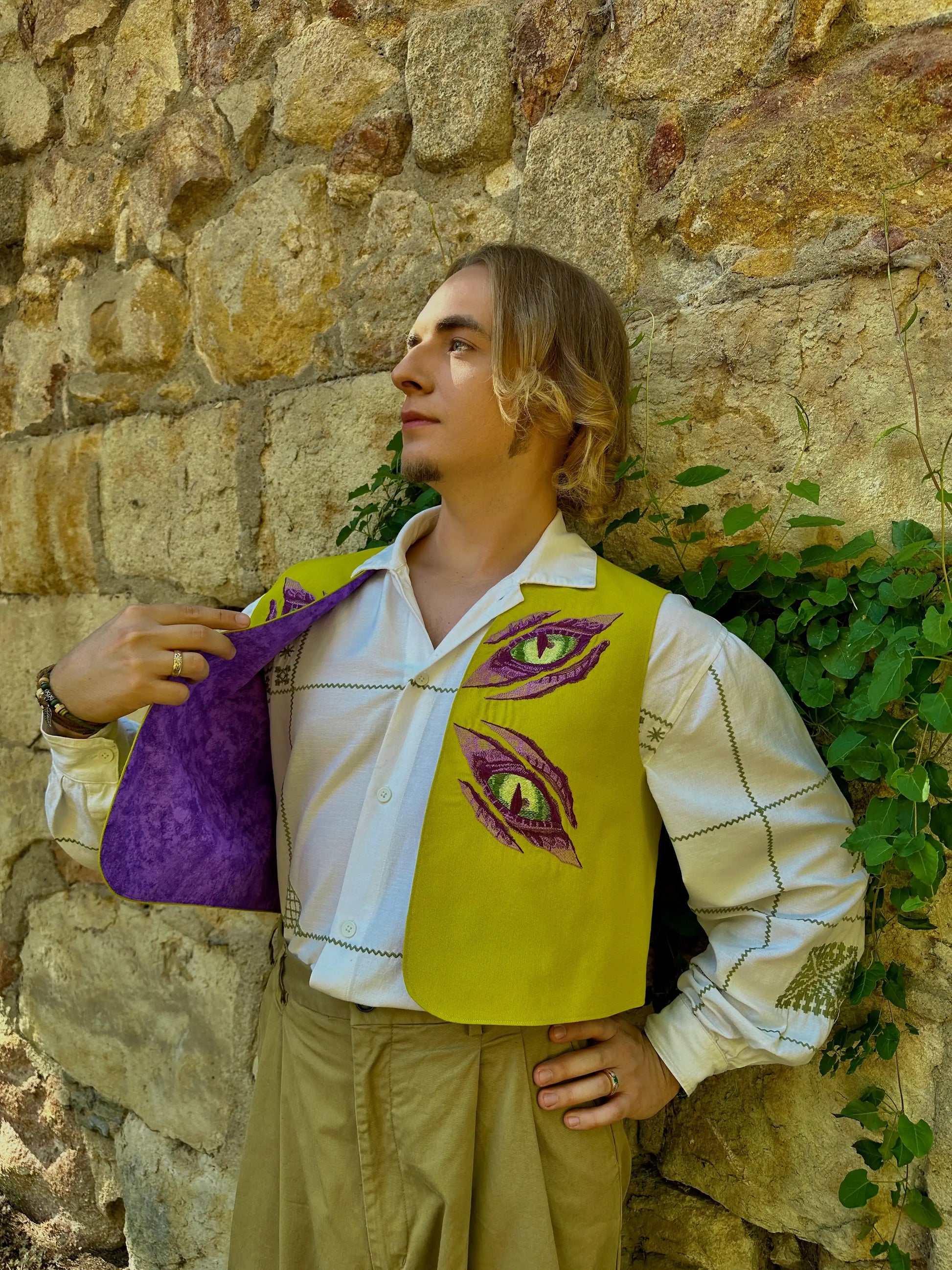 Person wearing a yellow vest with purple designs against a stone wall.