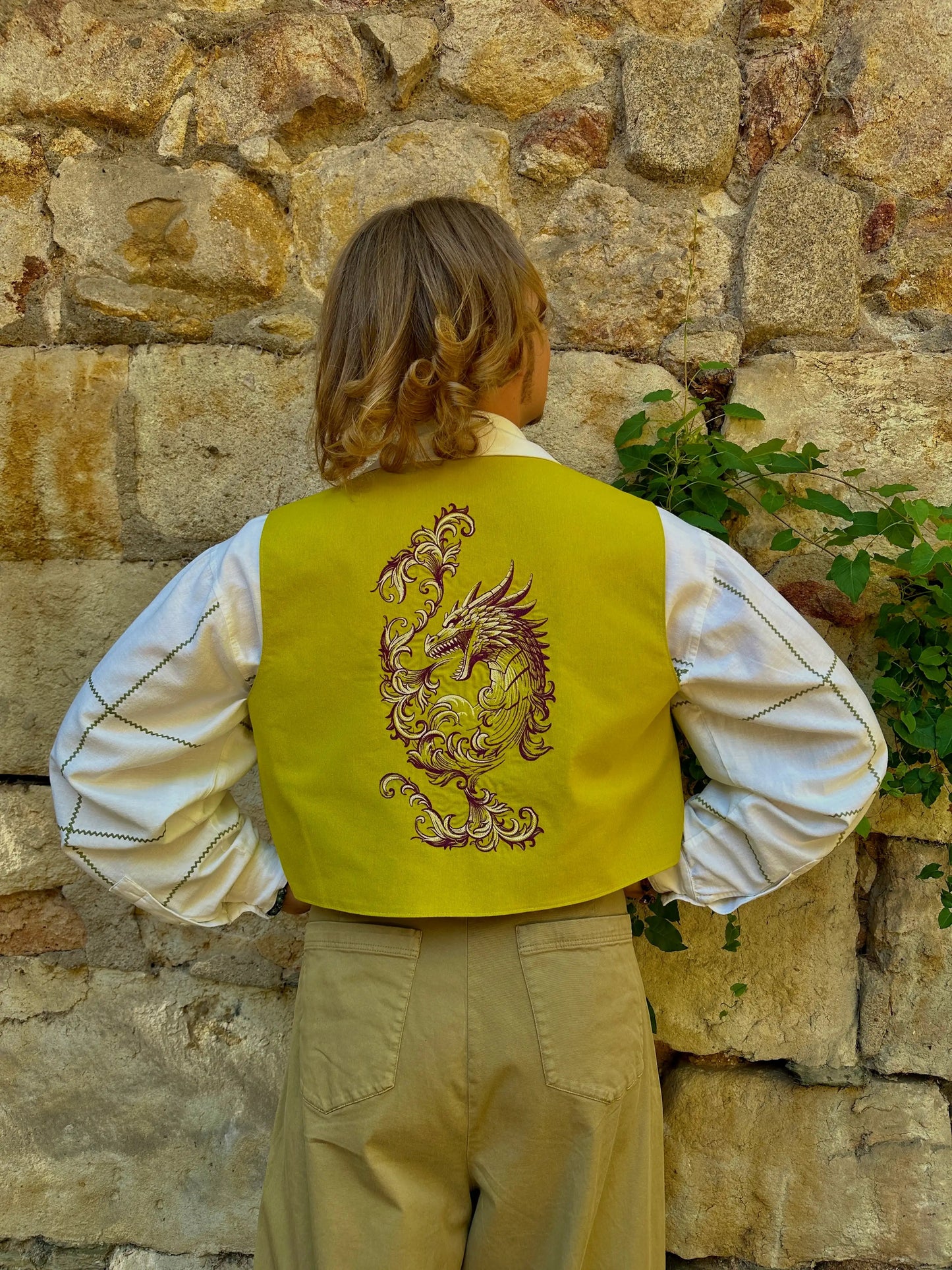 Person wearing a yellow vest with a dragon design against a stone wall.