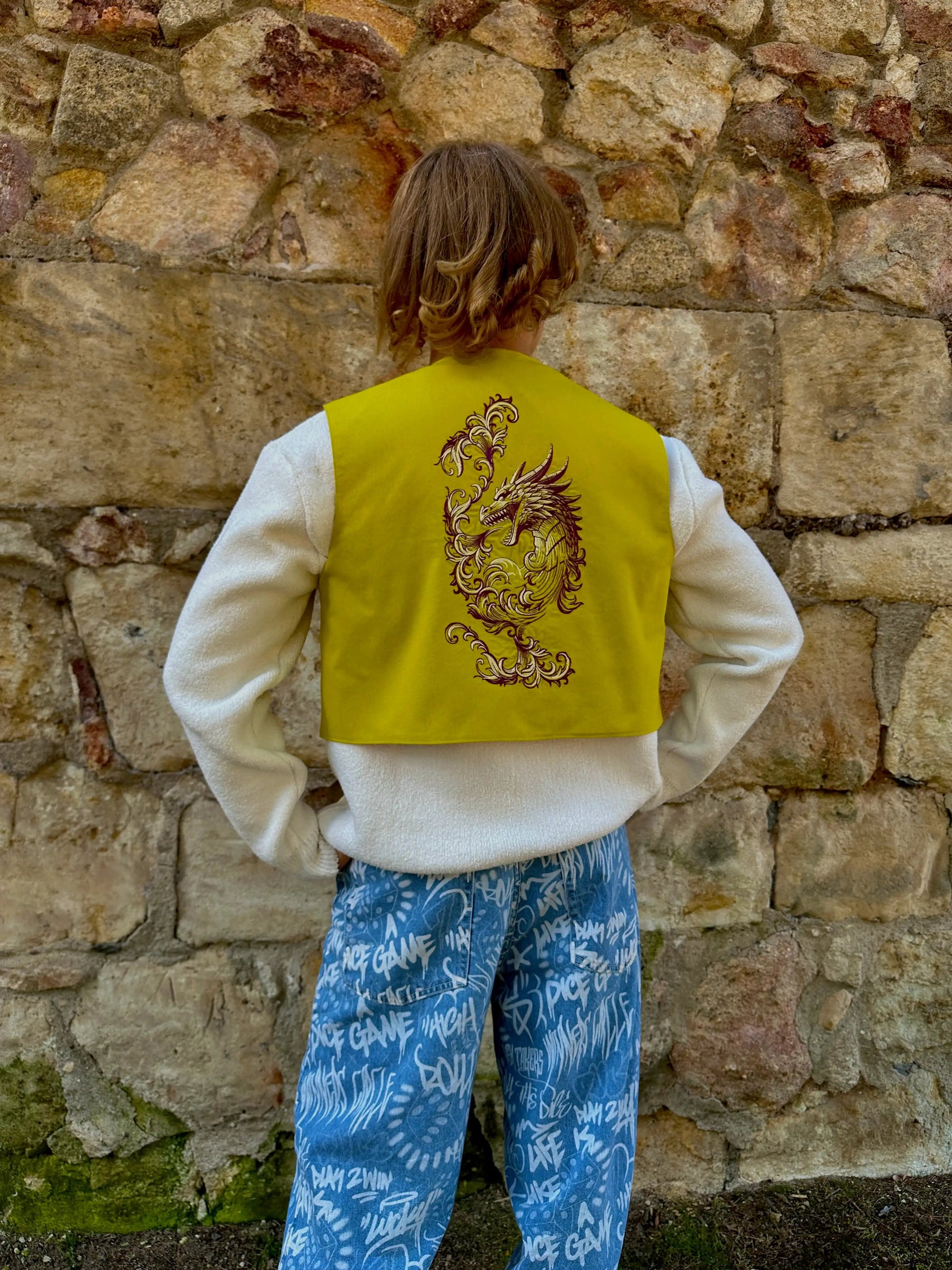 Person wearing a yellow vest with a dragon design against a stone wall.