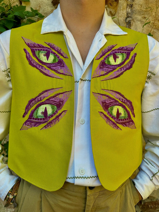 Person wearing a green vest with embroidered purple and green eyes design.