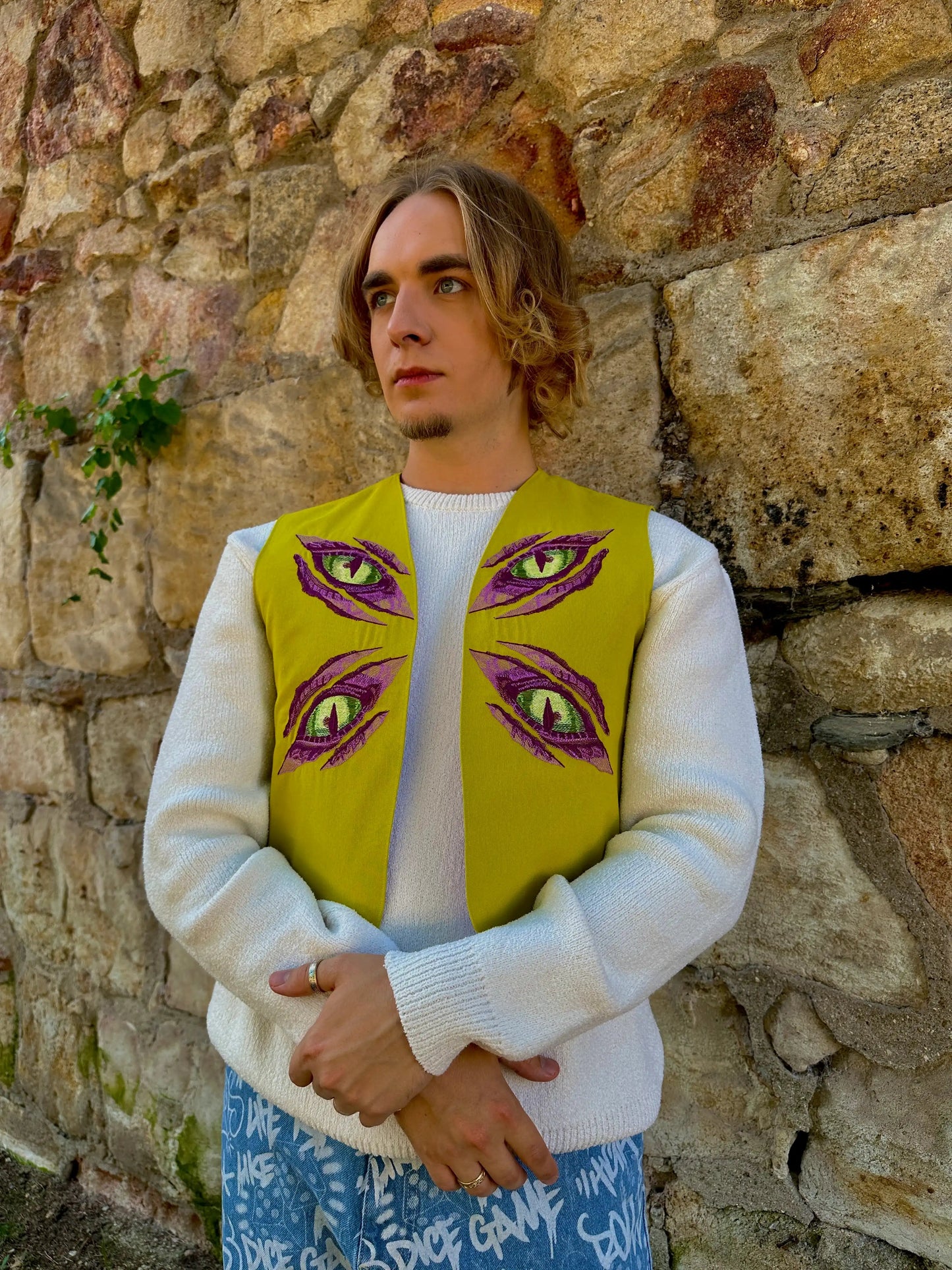 Person wearing a yellow vest with eye designs against a stone wall.
