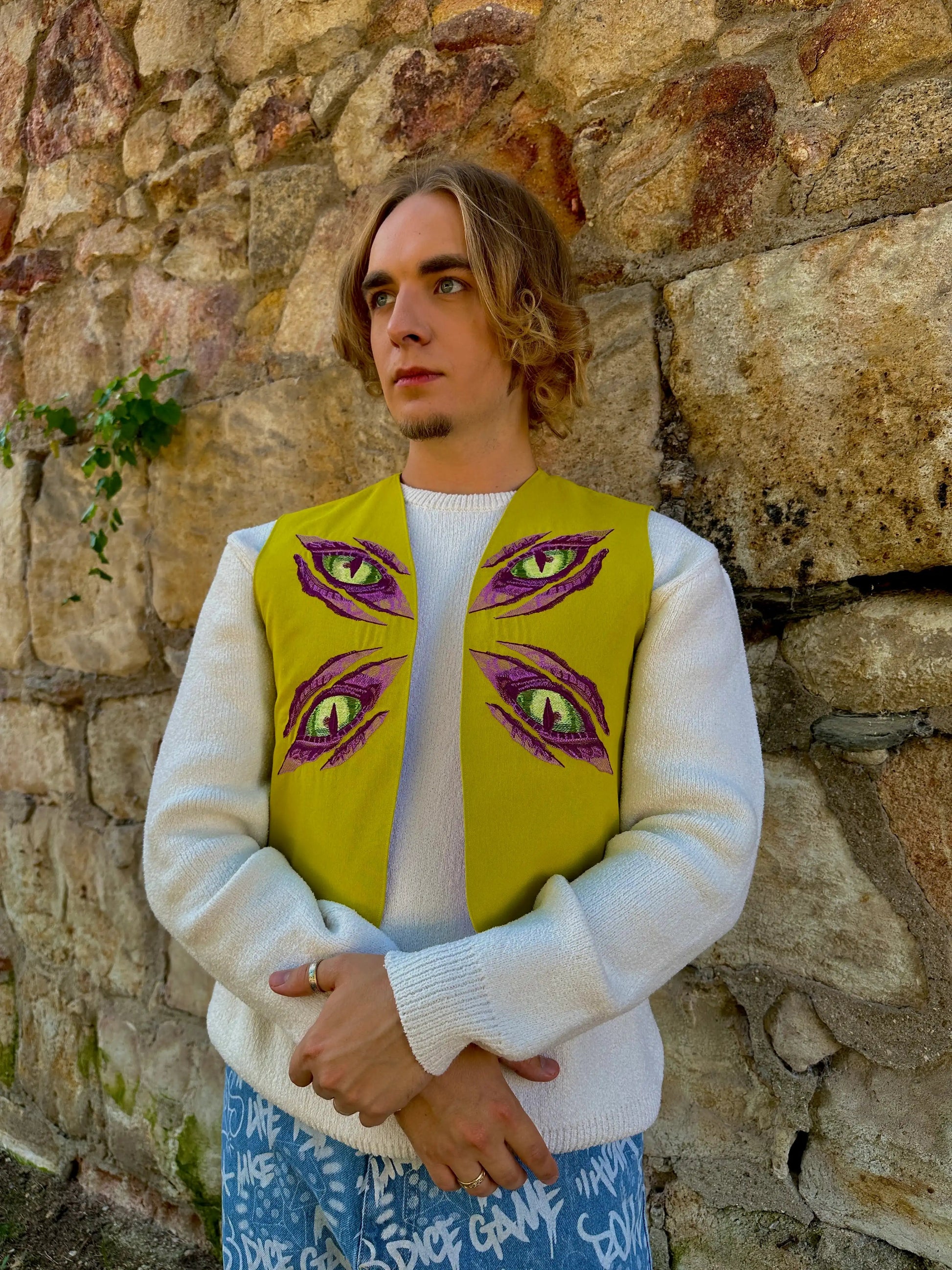 Person wearing a yellow vest with eye designs against a stone wall.
