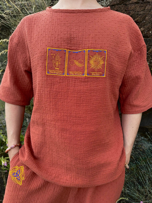 Person wearing a red textured shirt with embroidered designs in a natural setting