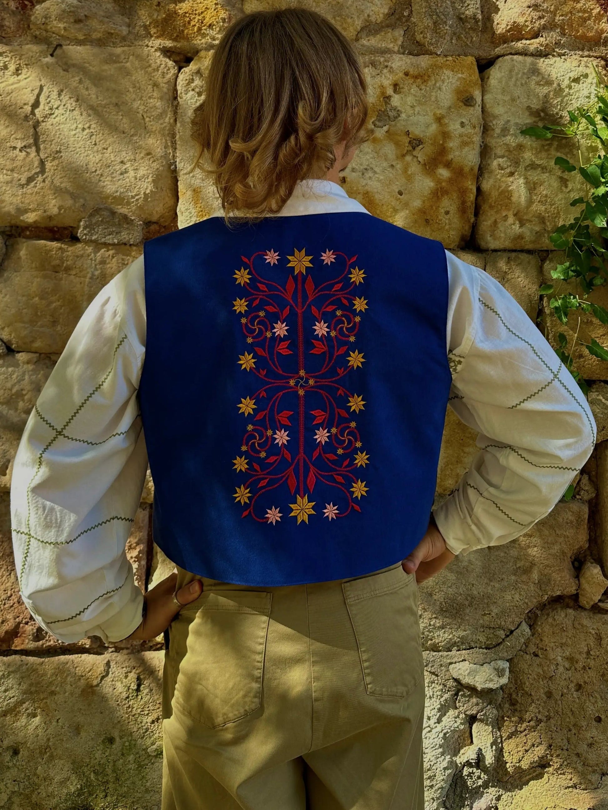 Person wearing a blue embroidered vest against a stone wall