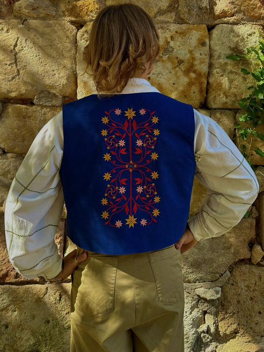 Person wearing a blue embroidered vest against a stone wall