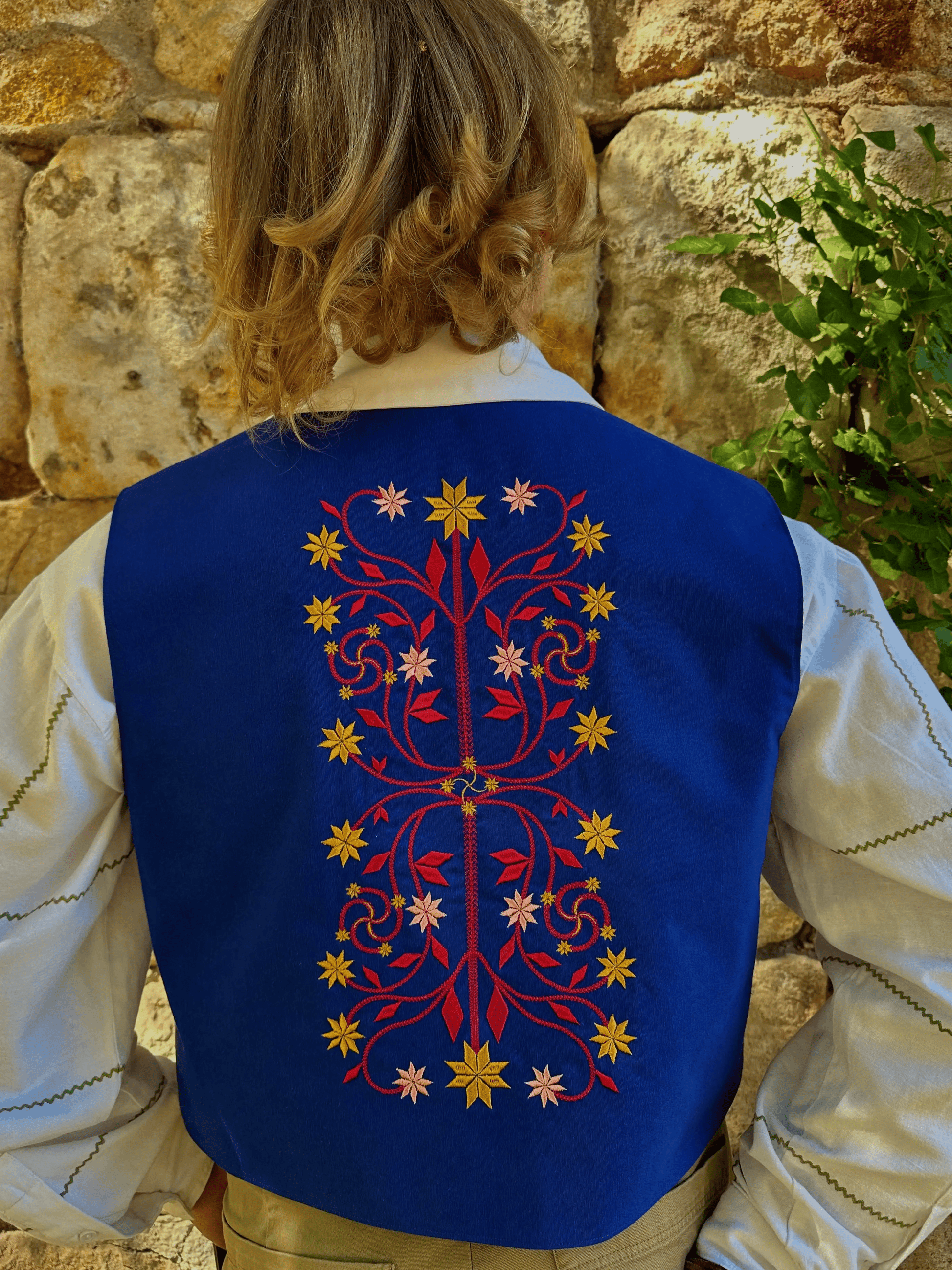 Person wearing a blue embroidered vest against a stone wall.
