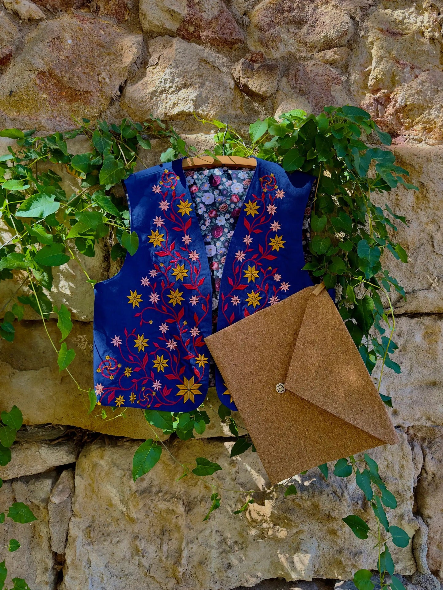 Floral-patterned vest and brown envelope against a stone wall with greenery