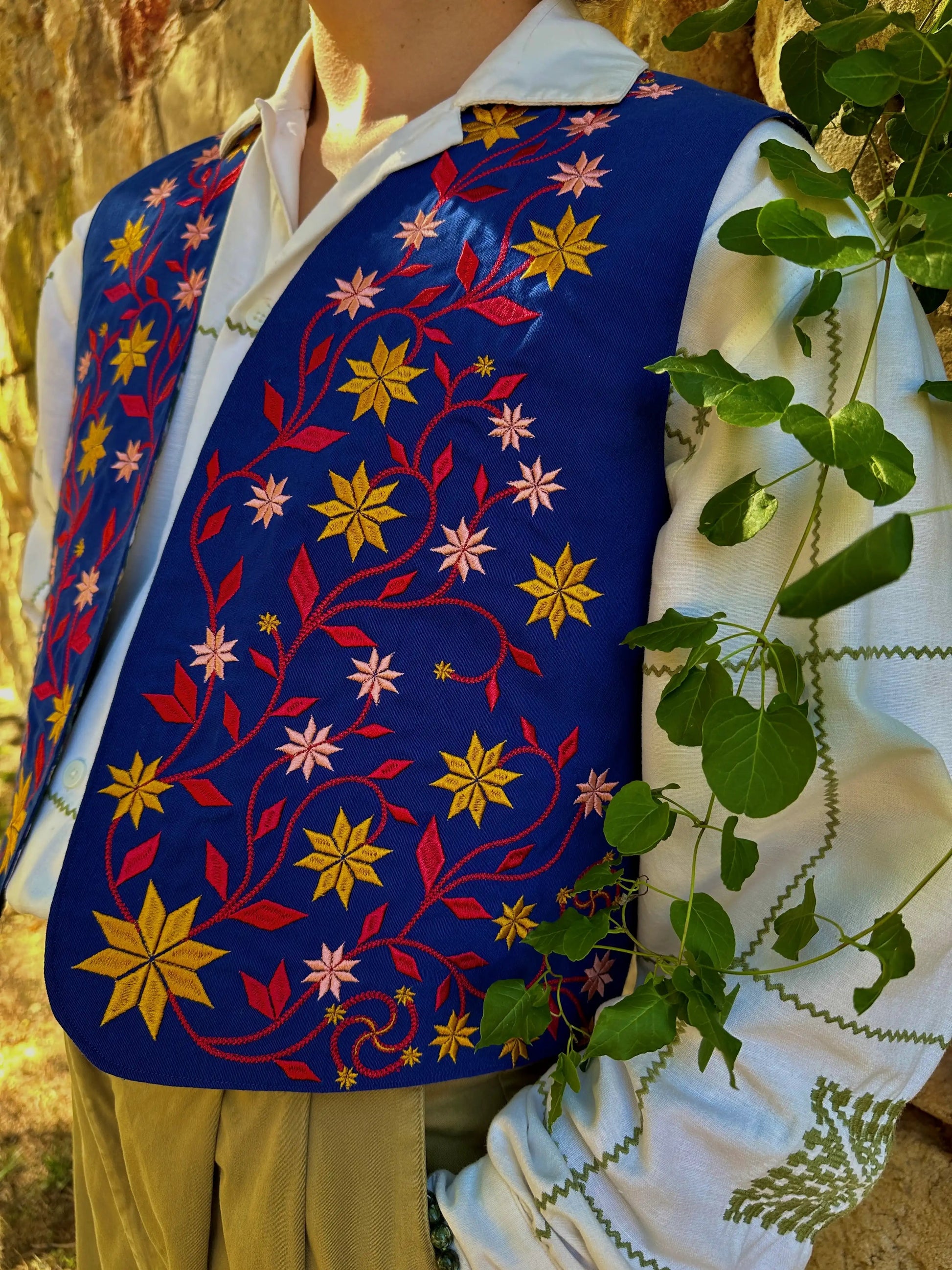 Person wearing a colorful embroidered vest with floral patterns in a natural setting.