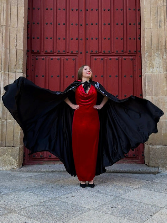 Woman in a red dress with a black cape standing in front of a large red door.