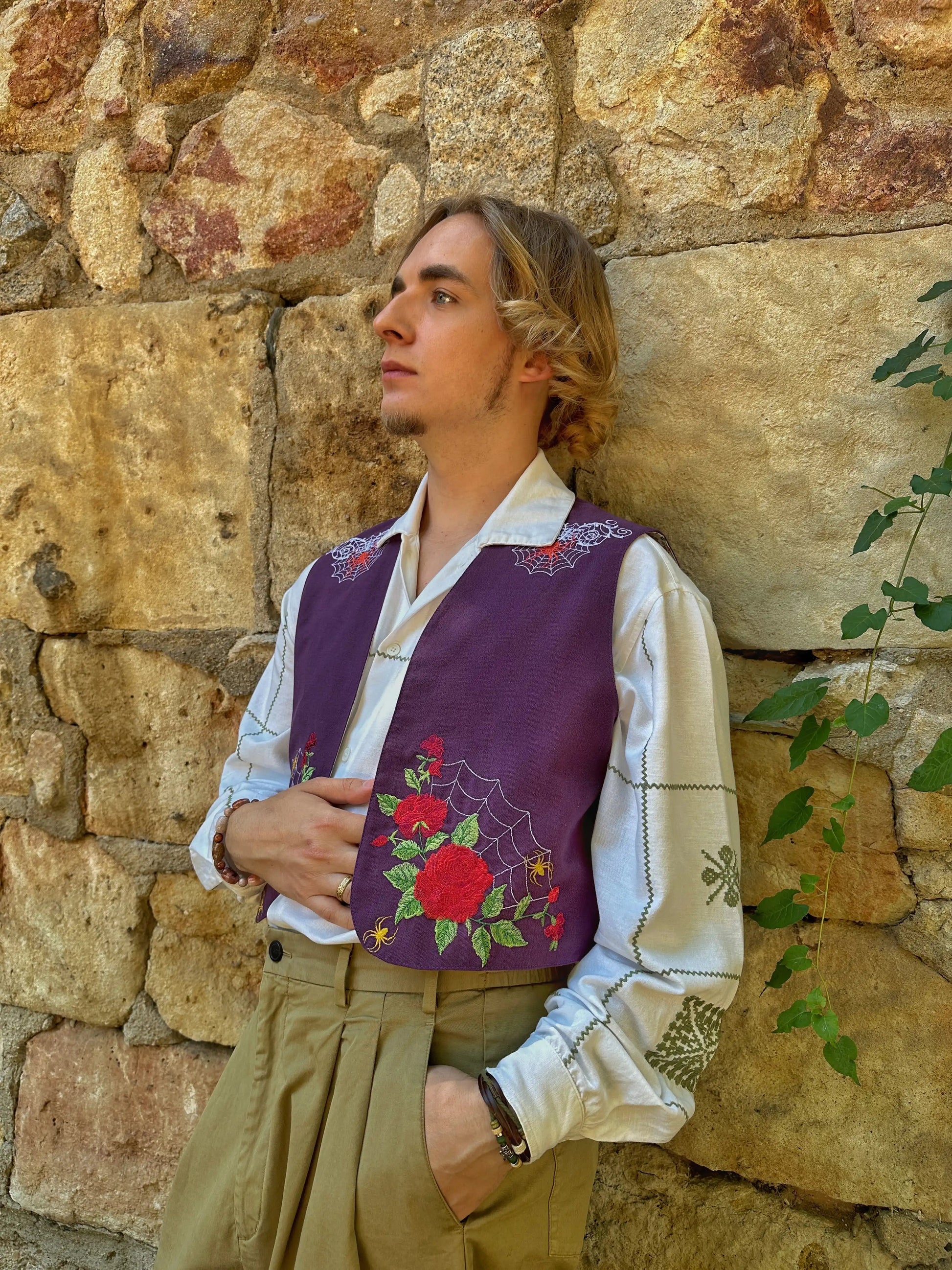 Person wearing a traditional embroidered vest against a stone wall
