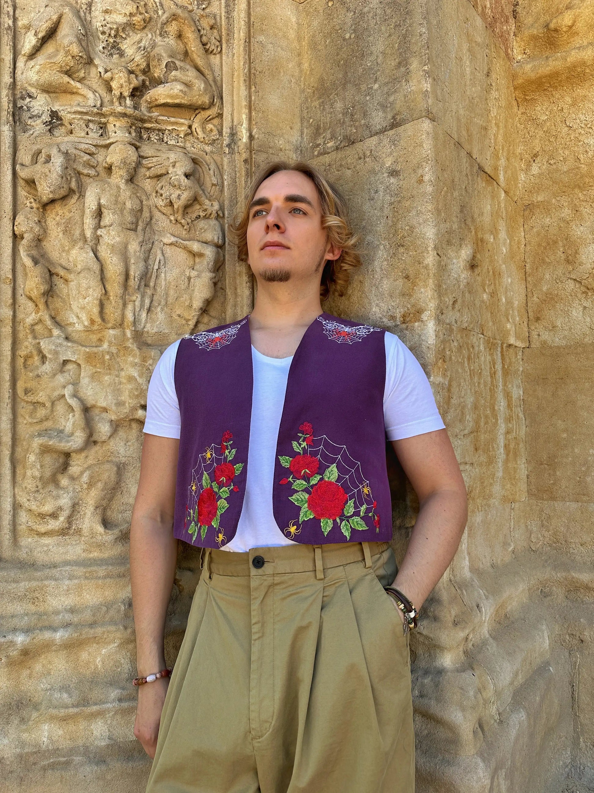 Person wearing a purple vest with floral patterns against a stone wall.