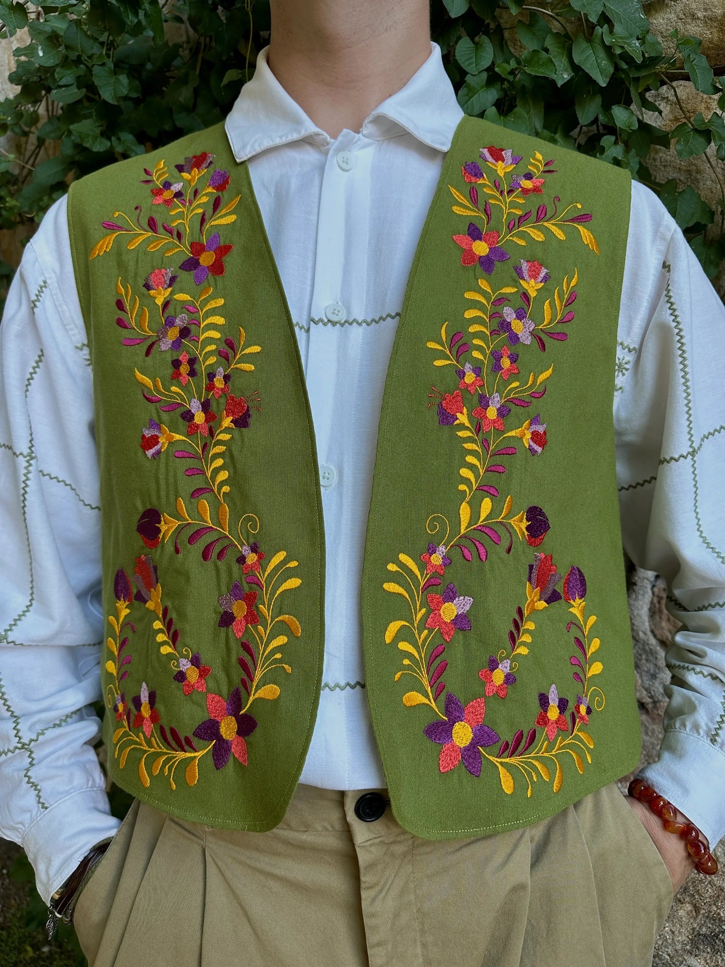 Green embroidered vest over a white shirt with a floral pattern, worn by a person.