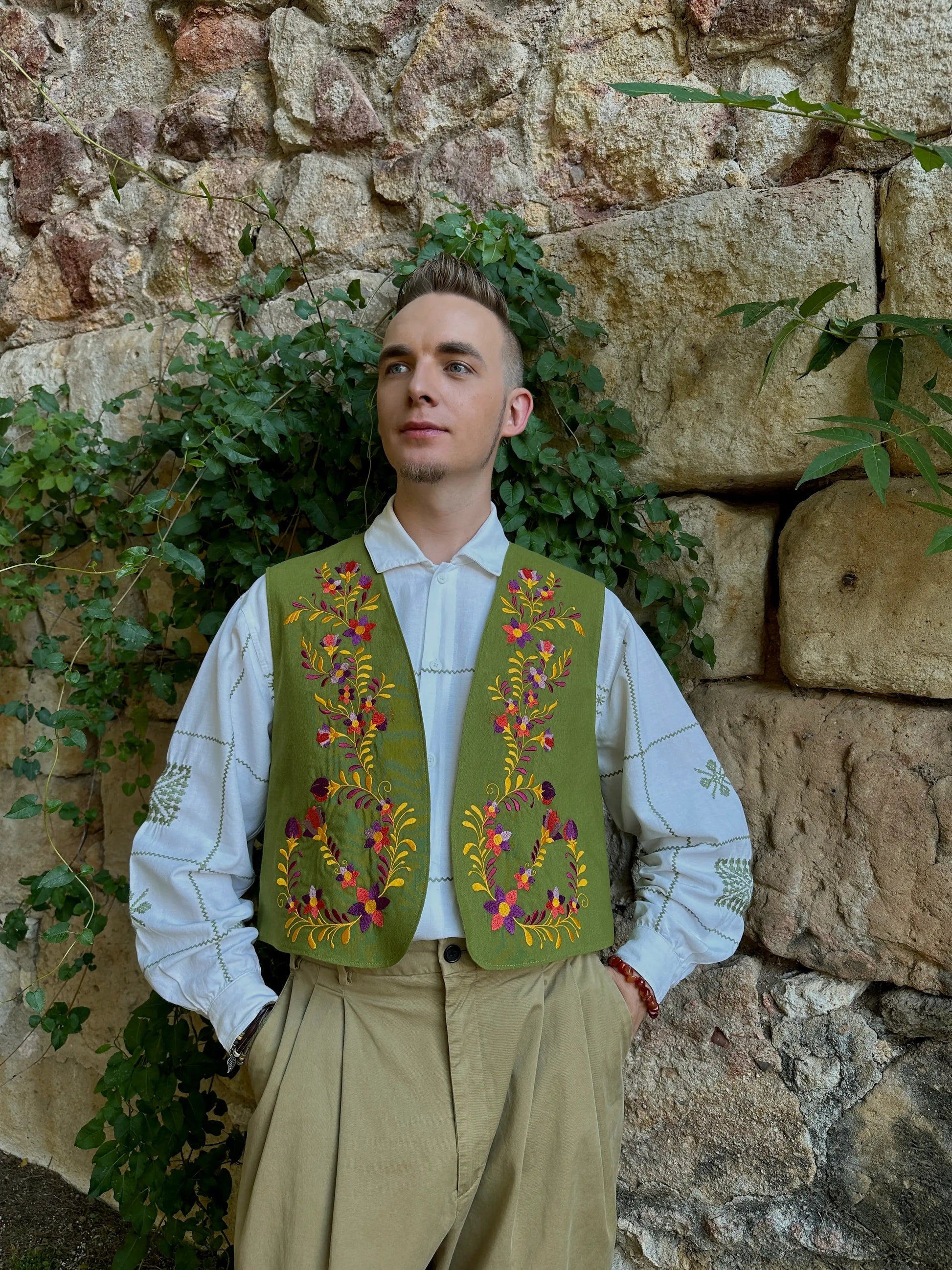 Person wearing a traditional embroidered vest against a stone wall