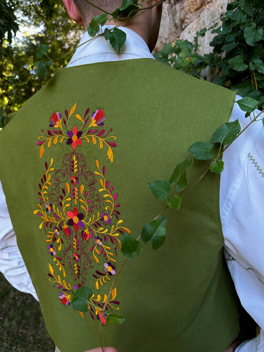 Green embroidered vest with colorful floral design worn by a person outdoors.
