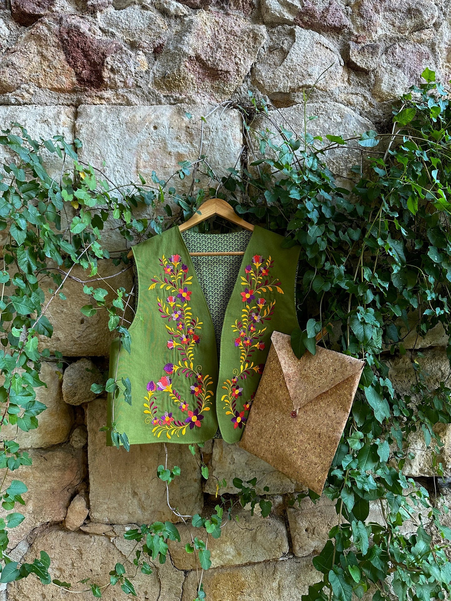 Green embroidered vest hanging on a stone wall with greenery