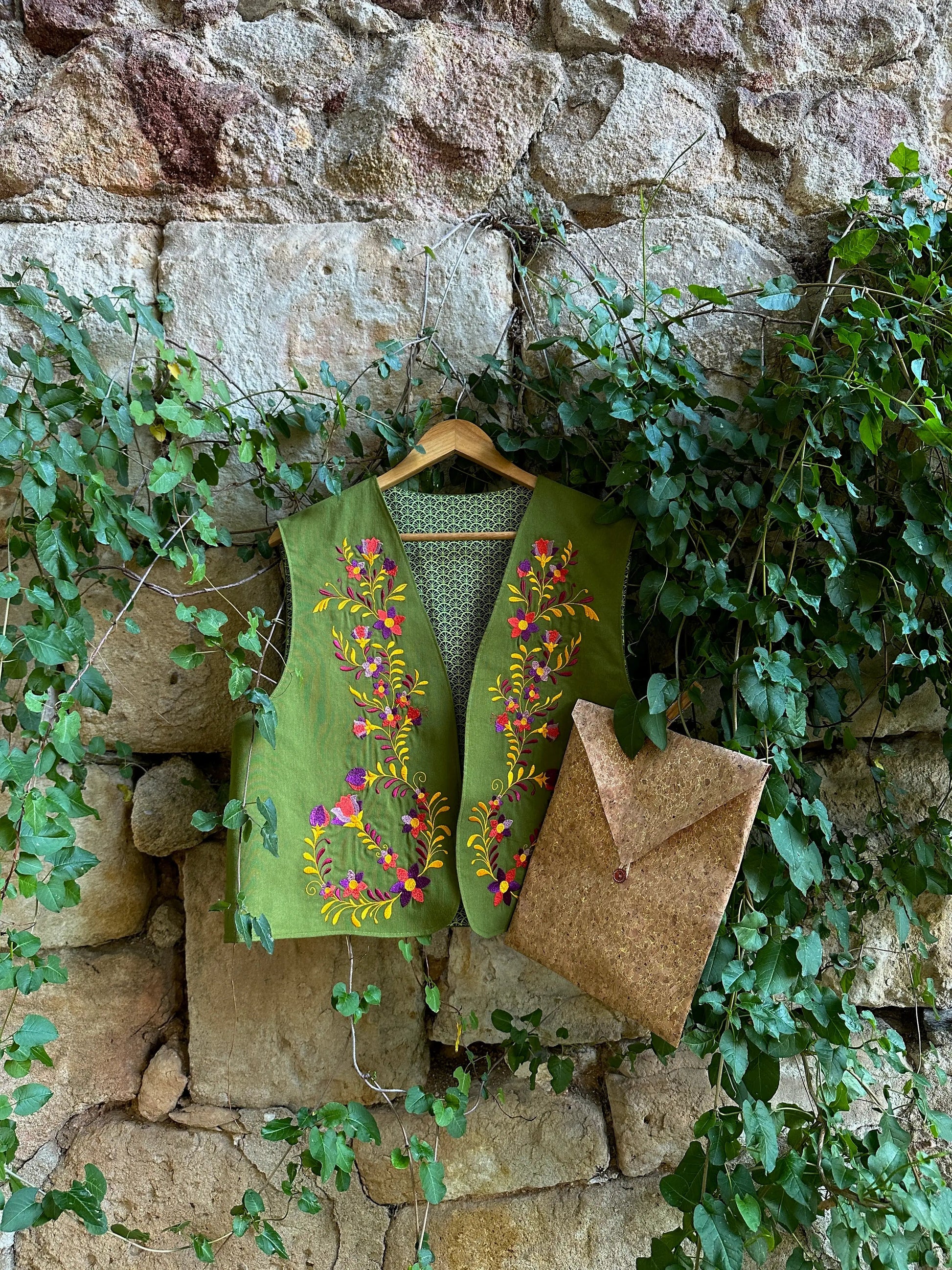 Green embroidered vest hanging on a stone wall with greenery