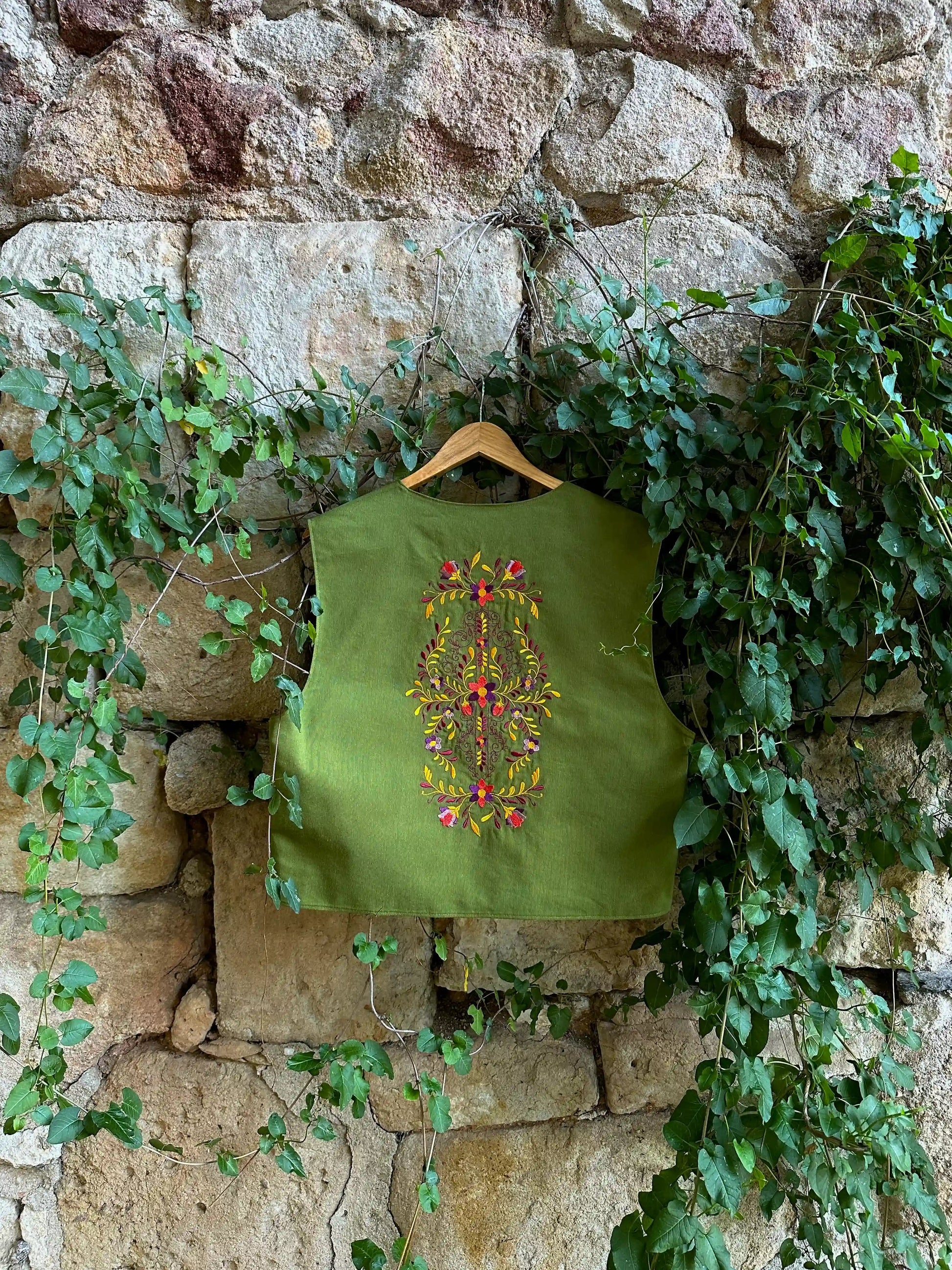 Green embroidered top on a hanger against a stone wall with greenery