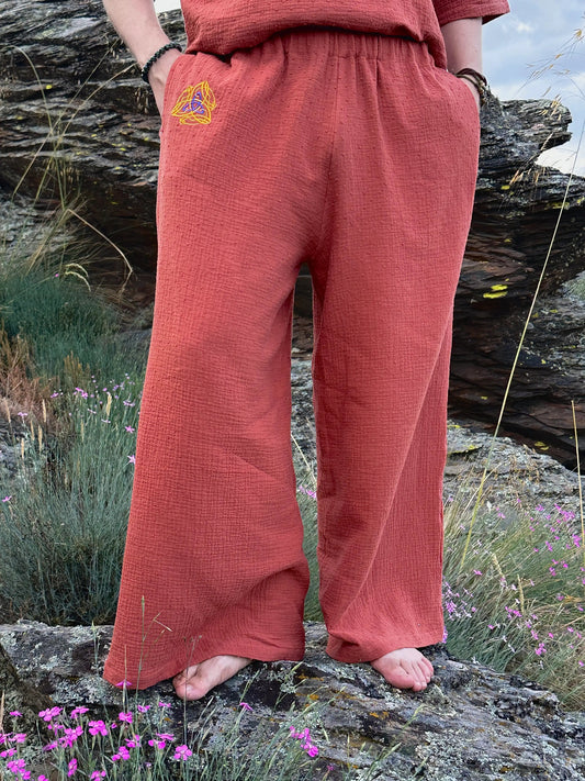 Person wearing red pants with a triangle emblem in a natural setting with rocks and flowers.