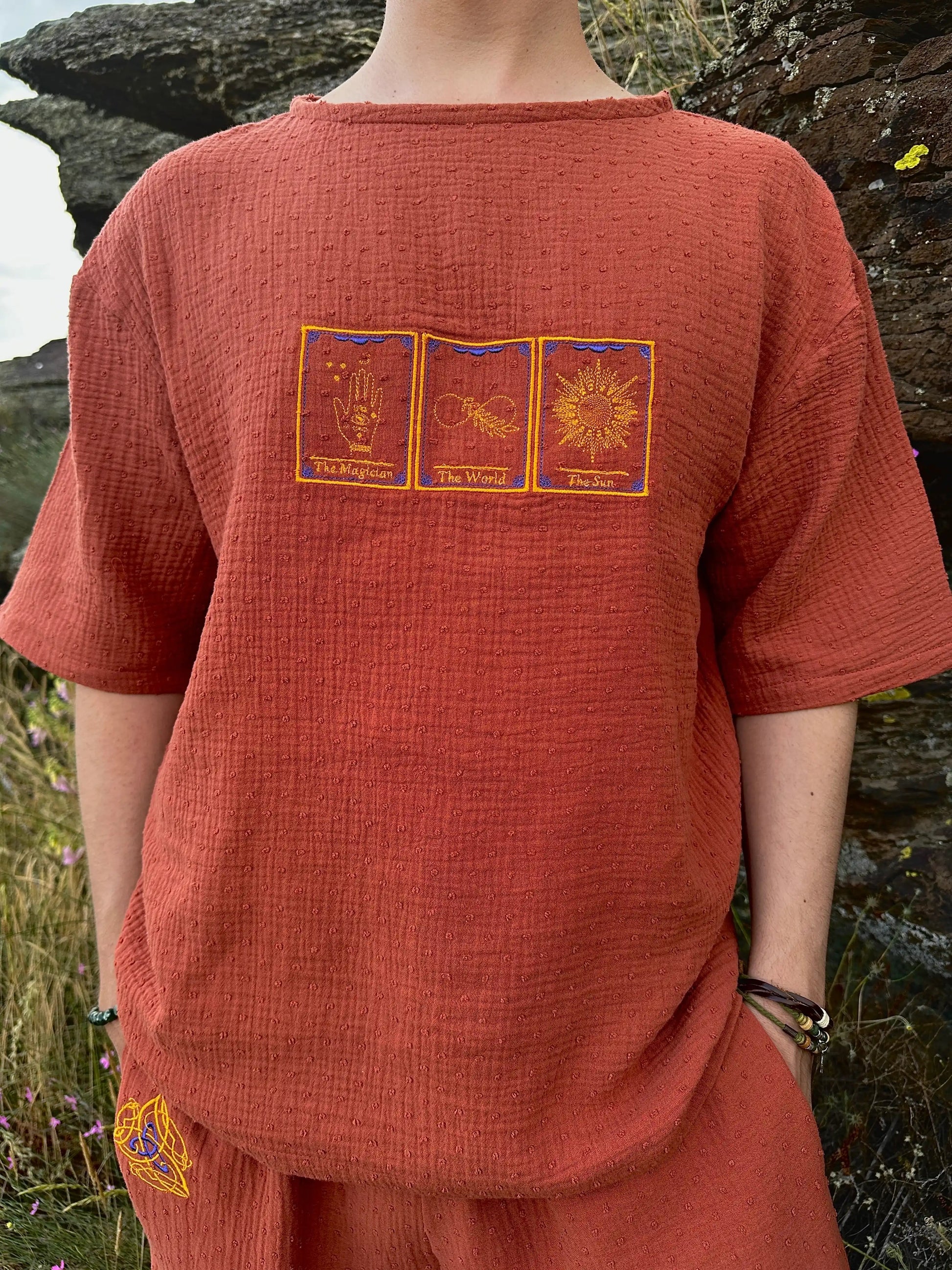 Person wearing a rust-colored outfit with embroidered designs in an outdoor setting