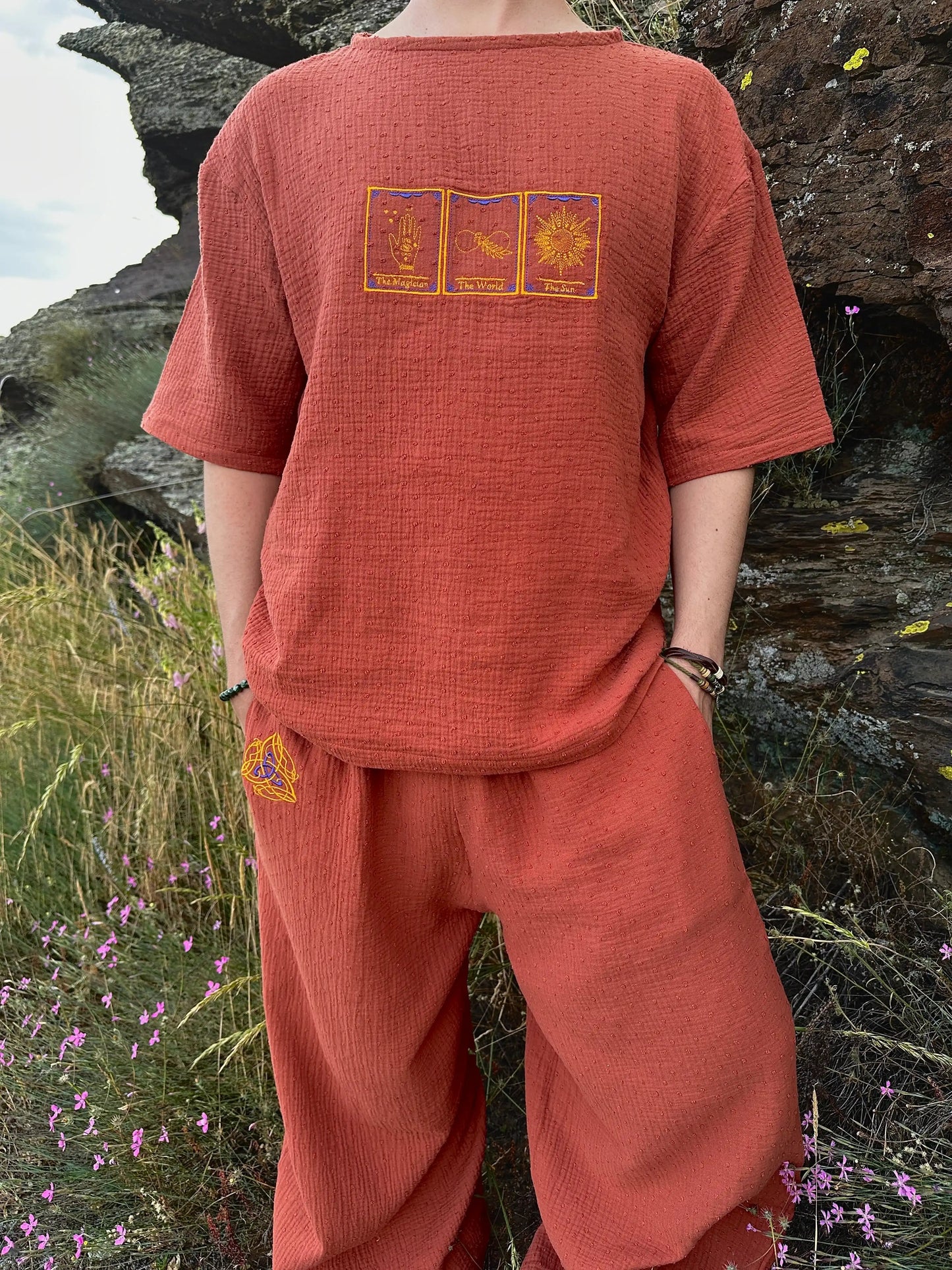 Person wearing a rust-colored outfit with embroidered designs in a natural setting
