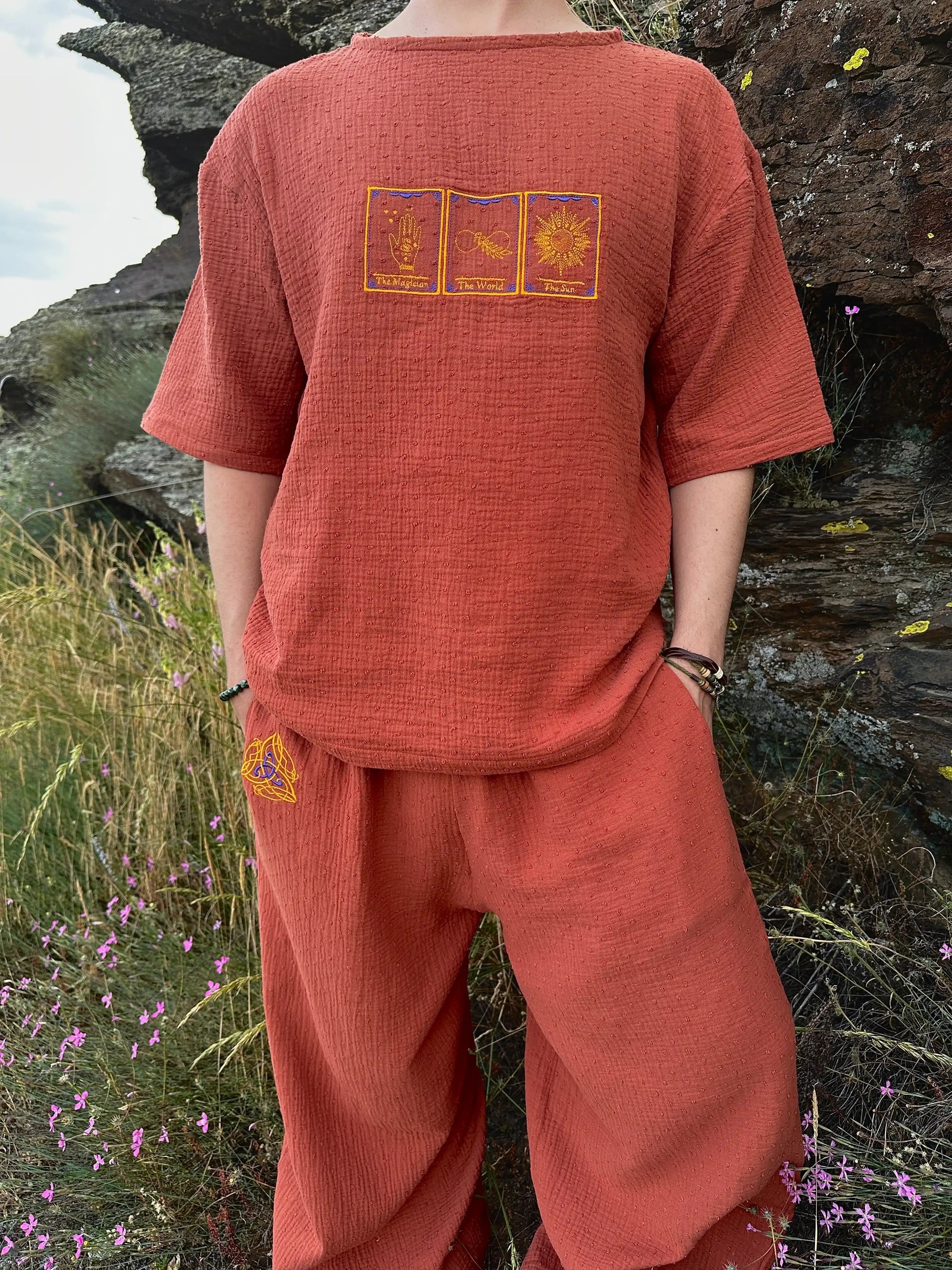 Person wearing a rust-colored outfit with embroidered designs in a natural setting