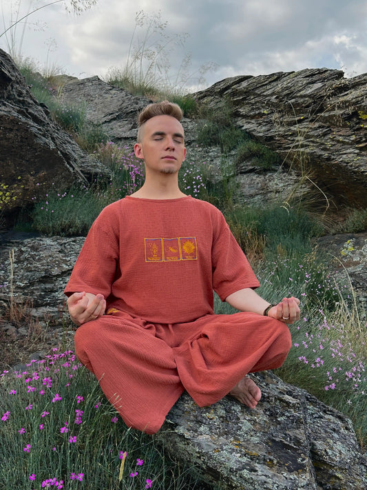 Person in a red outfit meditating on a rock with a natural landscape in the background