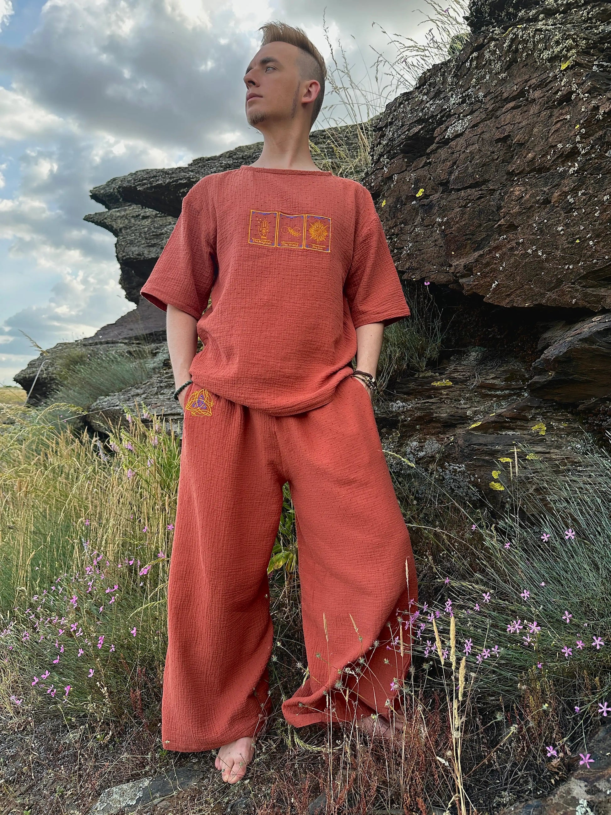Person wearing a red outfit standing in a natural setting with rocks and flowers.