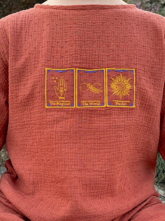 Red garment with embroidered tarot card designs on a blurred natural background