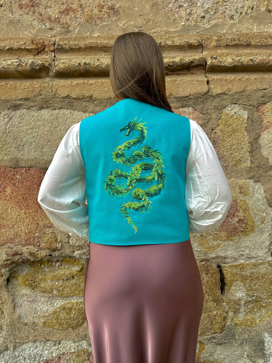 Person wearing a turquoise vest with a green dragon design against a stone wall.