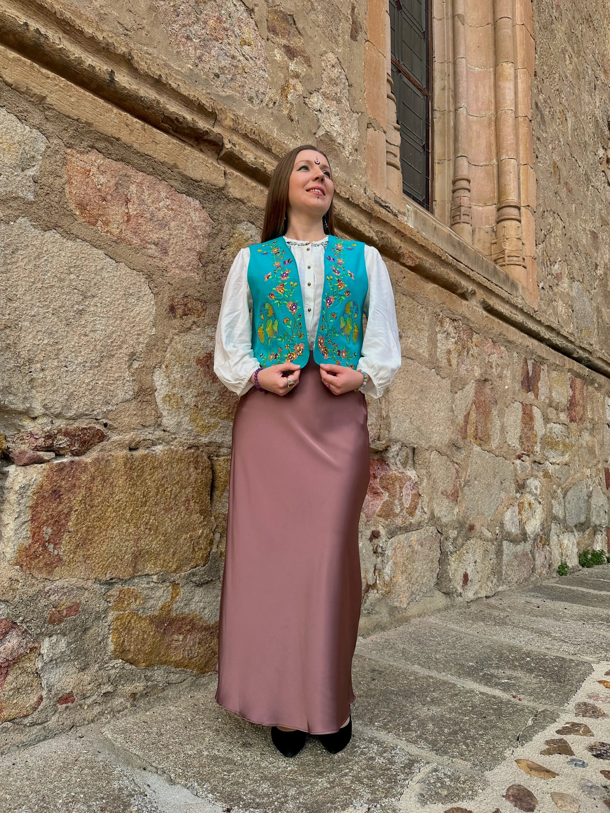Woman in traditional attire standing against a stone wall