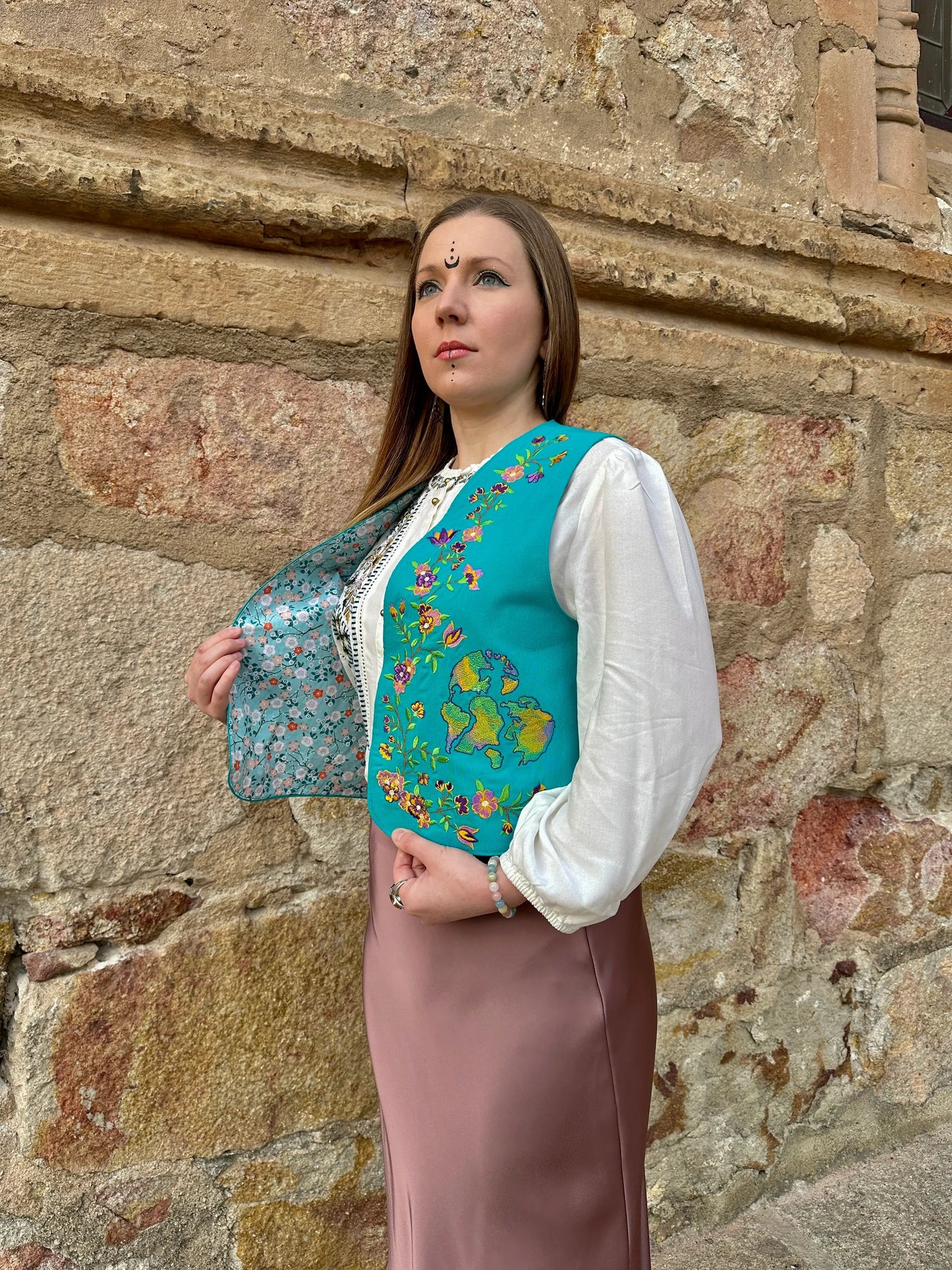 Woman in traditional attire standing against a stone wall