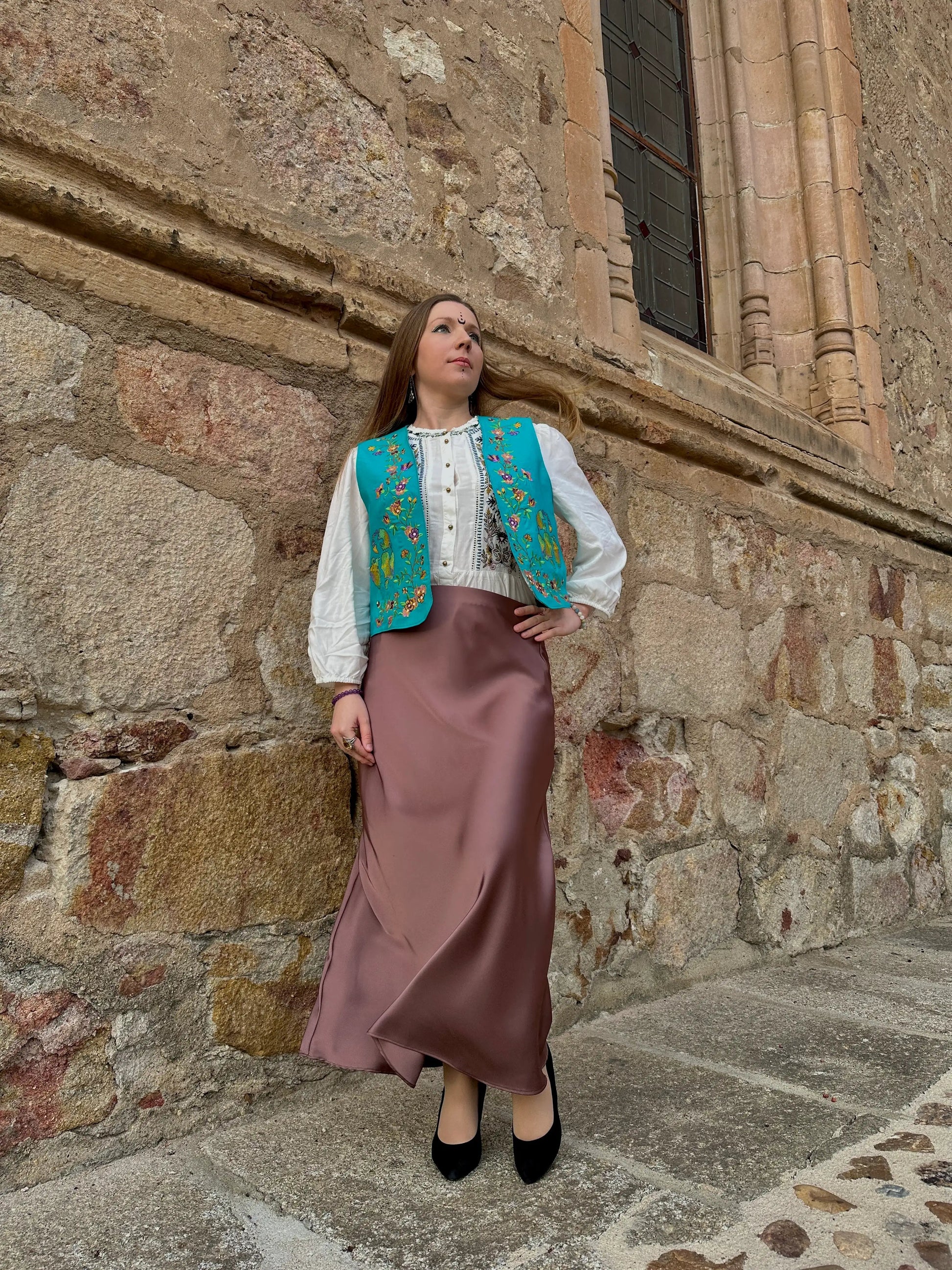 Woman in traditional attire standing against a stone wall