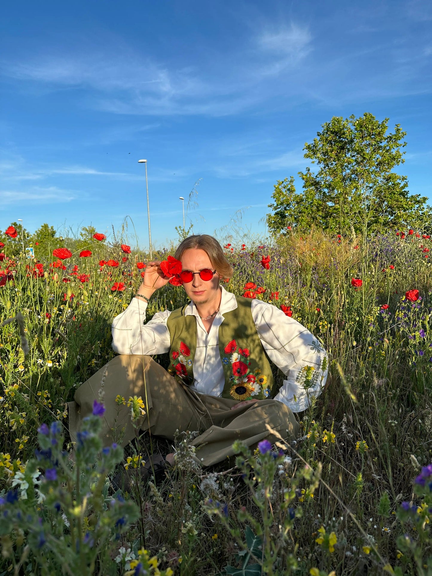 Person sitting in a field of flowers with a blue sky and trees in the background